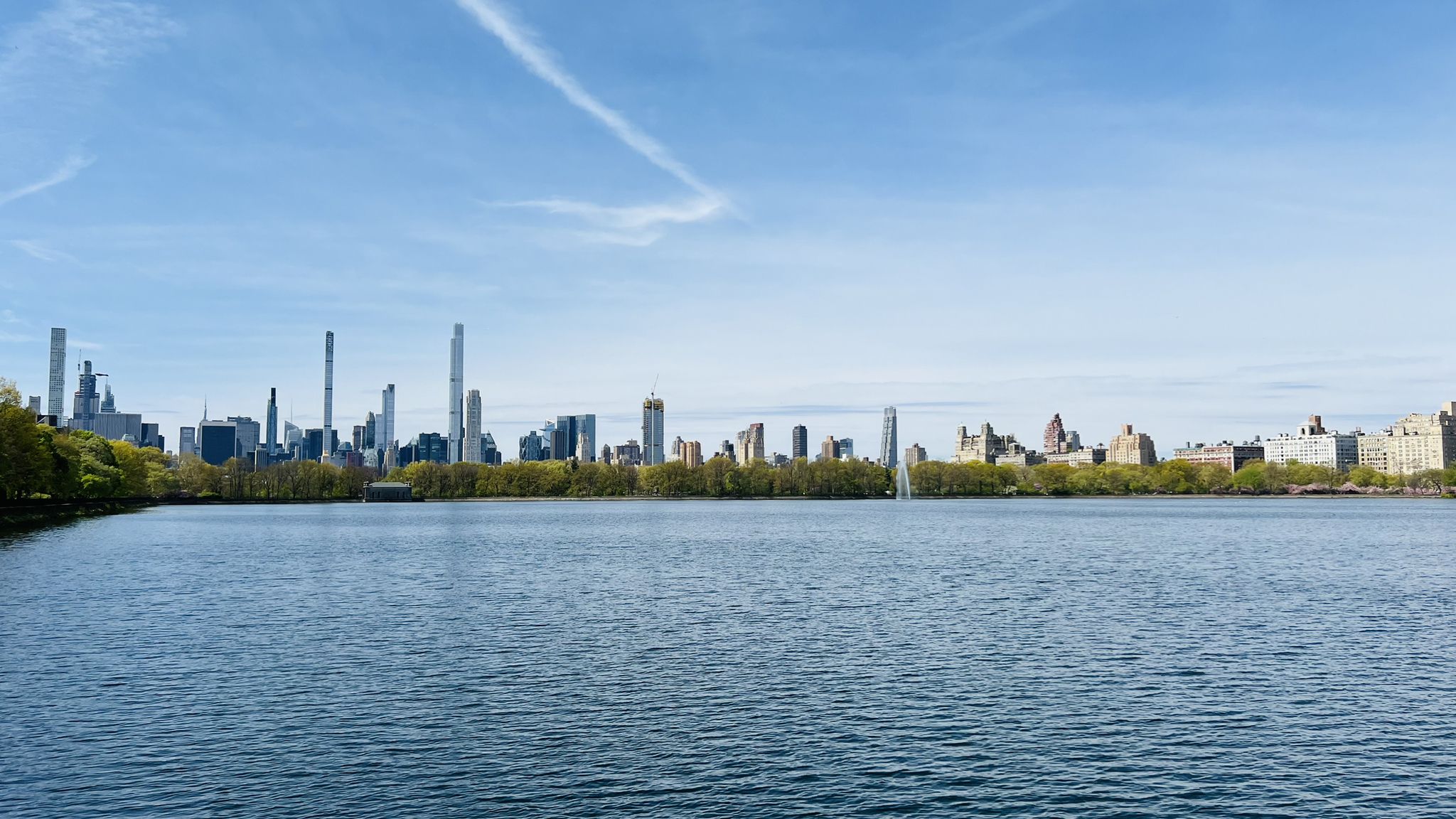 Wide lake with a distant city skyline under a blue sky. - View of the San Remo Towers – Bethesda Fountain and Terrace loop from 66th Street–Lincoln Center