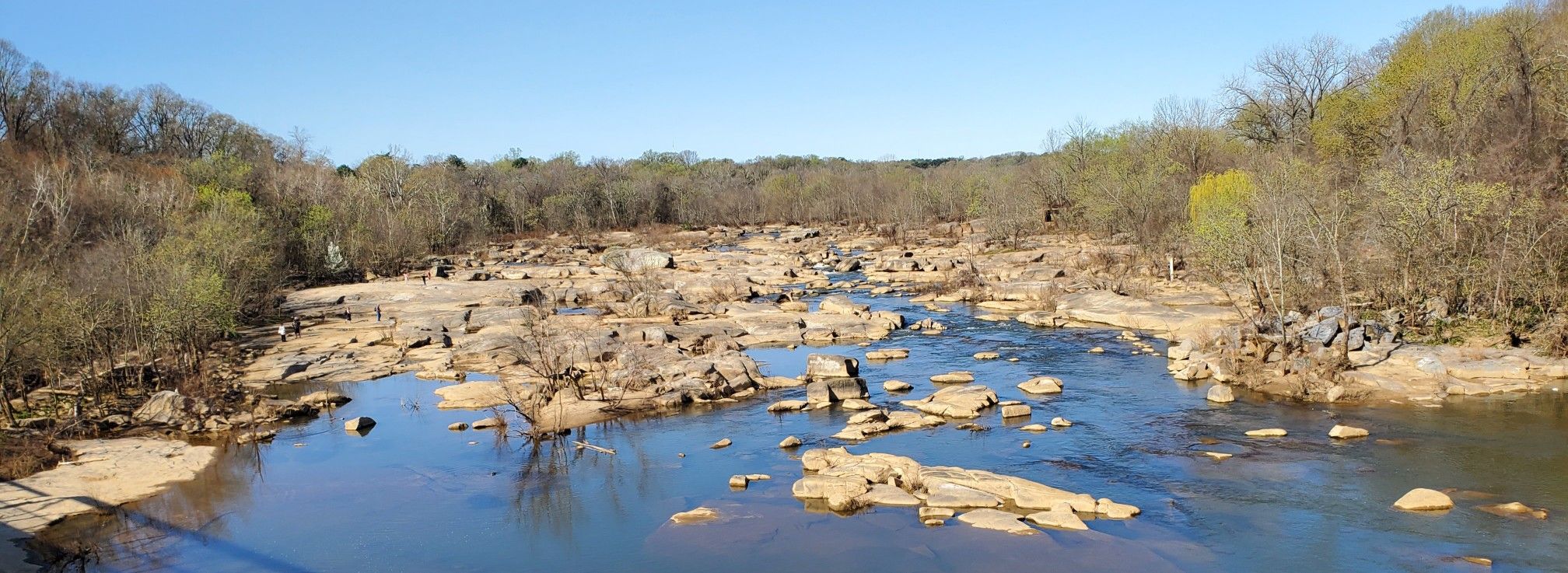 Wide river with many exposed rocks and small rapids, flanked by bare trees. - Buttermilk and North Bank Trail Loop