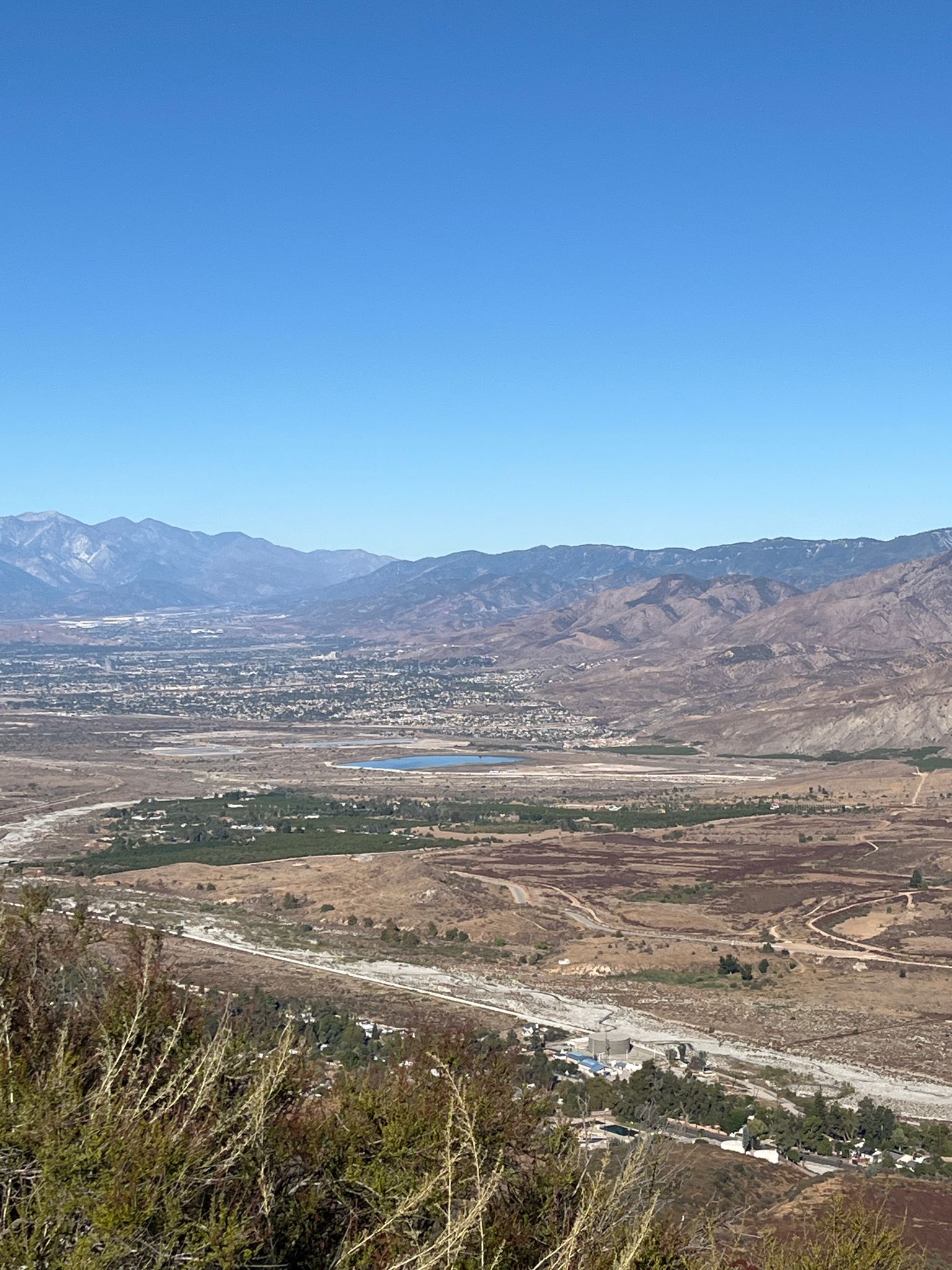 Panoramic view of a wide valley with a city, lake, and distant mountains. - Crafton Hills and Zanja Peak Loop