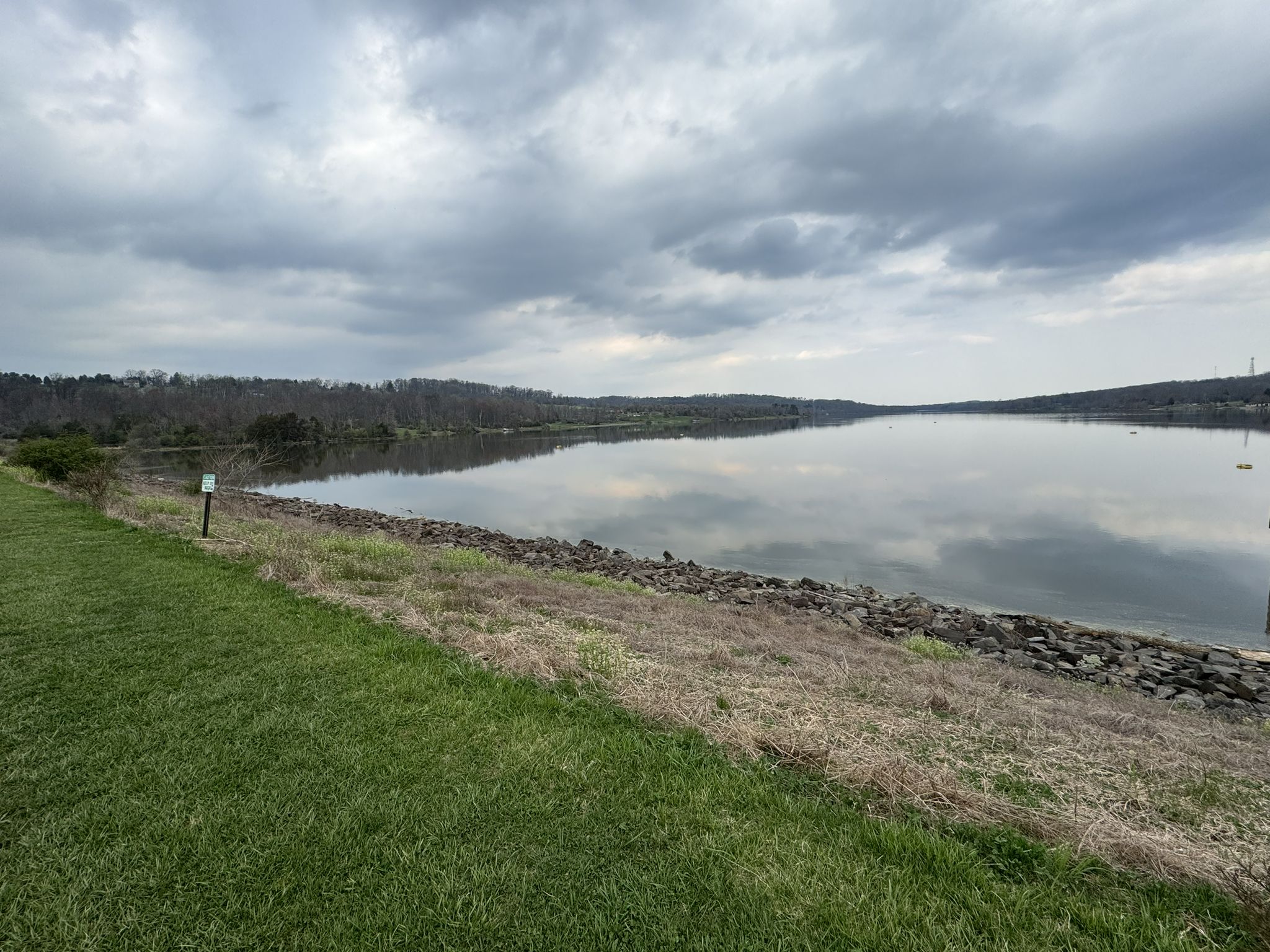 Overcast day over a calm lake reflecting clouds, with rocky and grassy shores. - Lake Galena Hike and Bike Trail