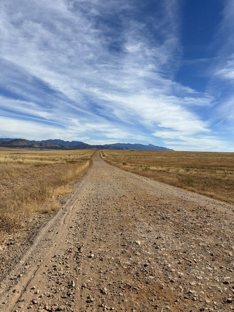A long dirt road through dry grasslands under a bright, cloudy blue sky. - Spirit World 50 Course loop — Gravel