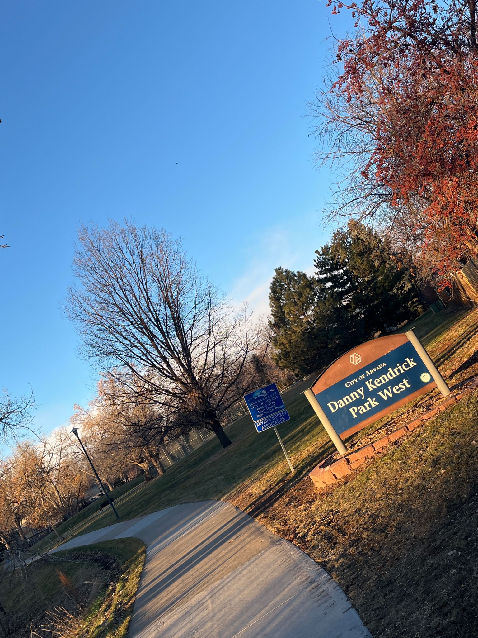 A park sign next to a paved path with bare trees under a blue sky. - Bike loop from Kipling St & W 48th Ave