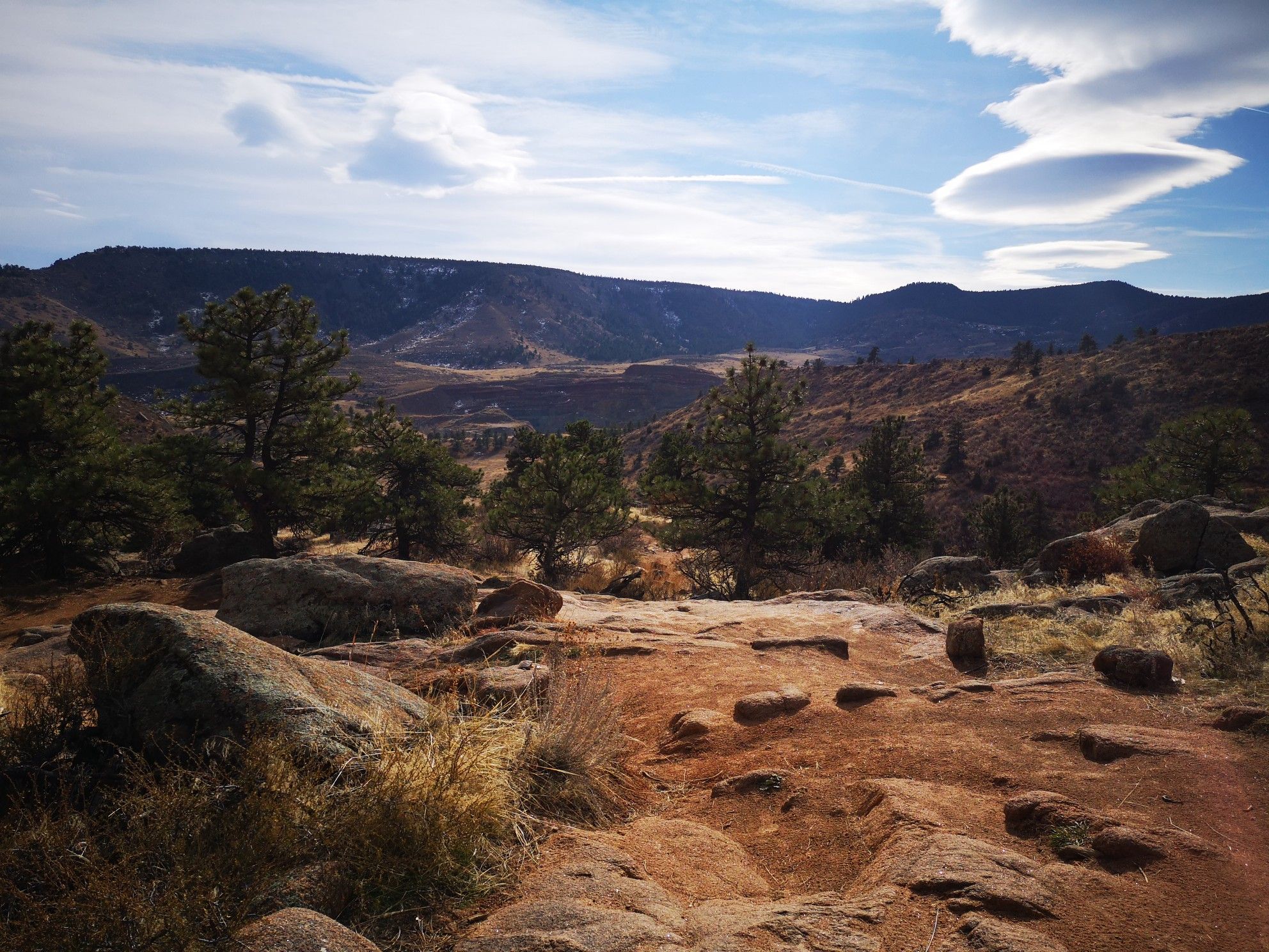 Rocky, arid landscape with scattered trees, distant mountains, and a cloudy sky. - Hall Ranch Loop