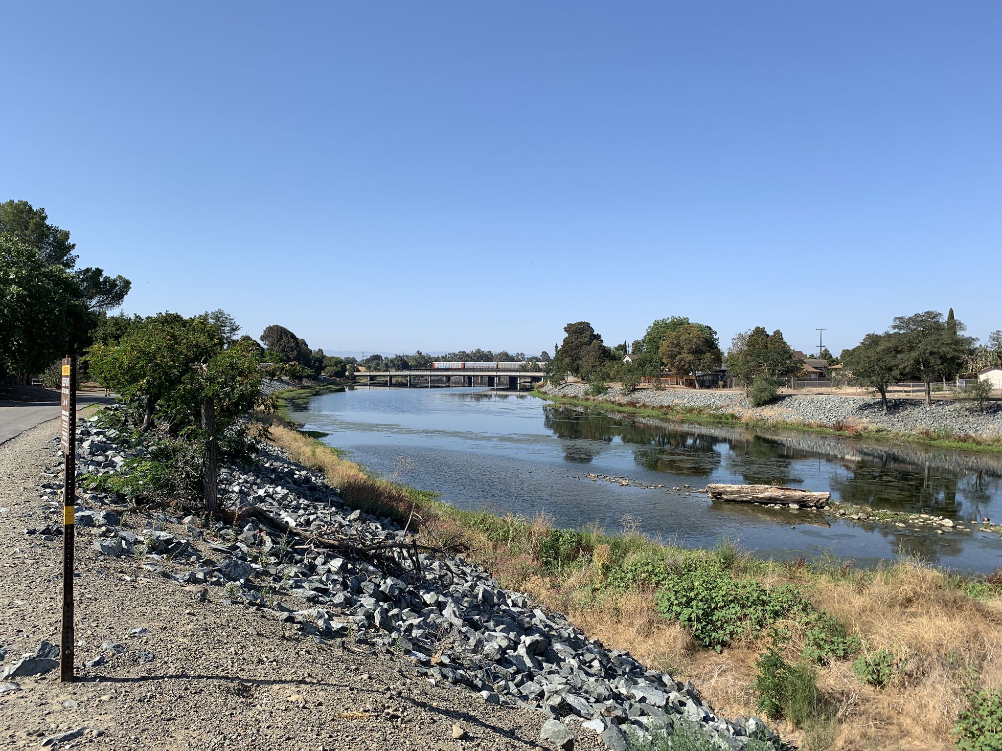 Wide river with a distant bridge, surrounded by green trees under clear sky. - Alameda Creek Regional Trail and Quarry Lakes Loop