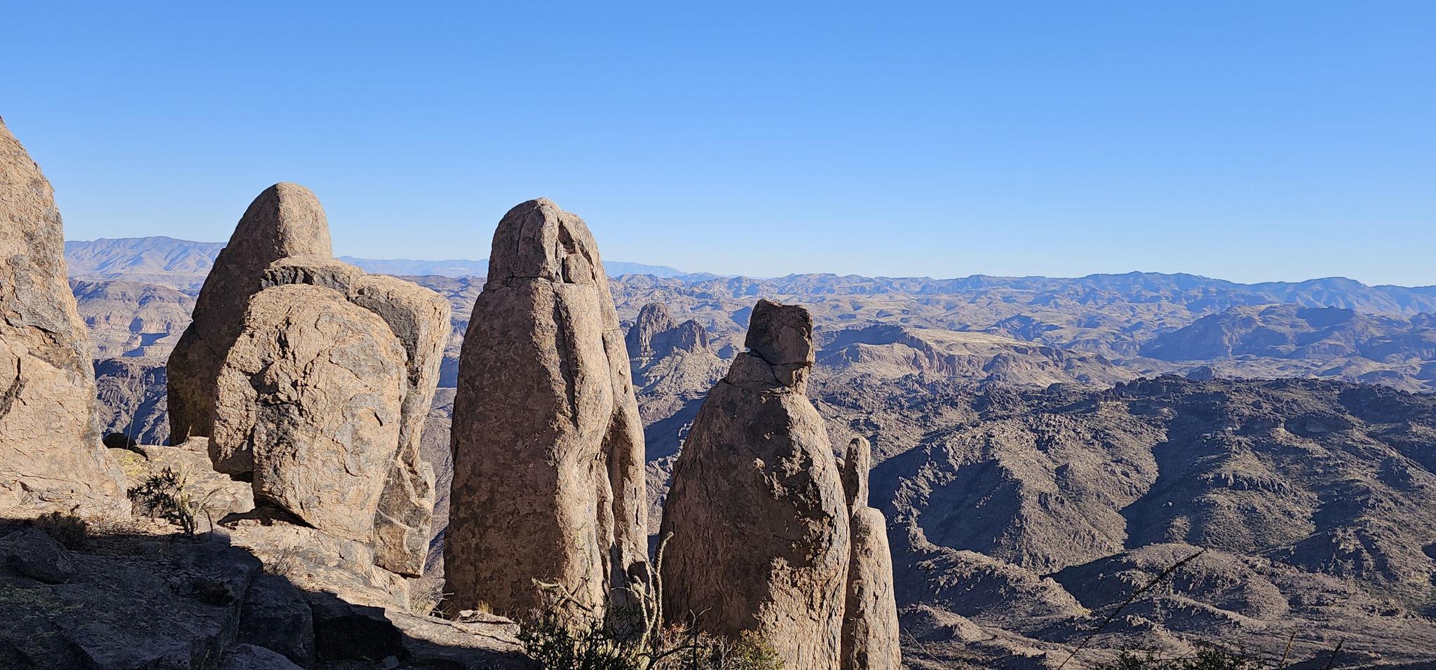 Three distinct rock spires stand tall against a vast mountain backdrop. - Superstition Peak via Carney Springs Trail