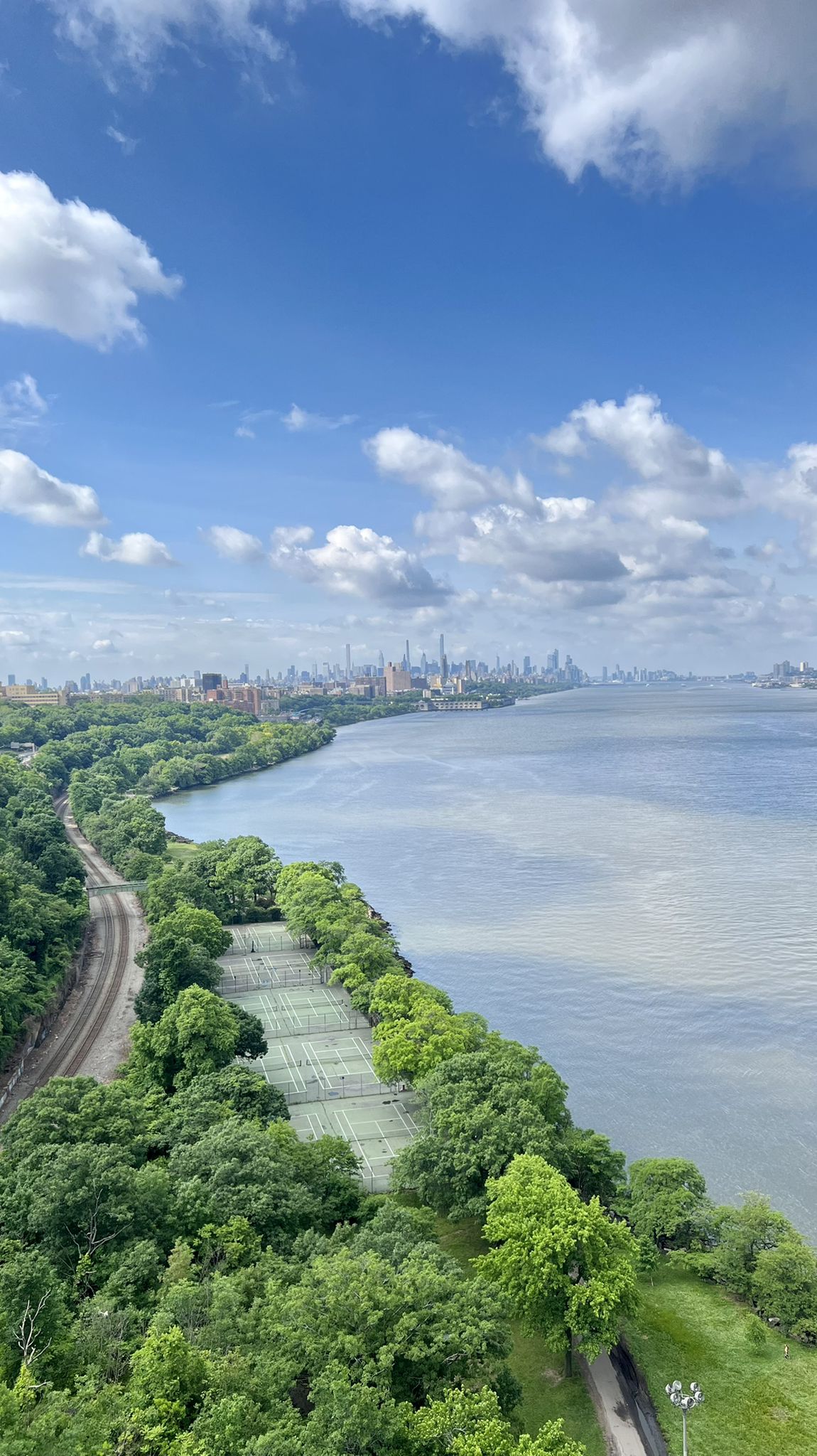 Wide river, distant city, green trees, and tennis courts under a cloudy sky. - South County Trailway – Van Cortlandt Greenway loop from Spring Valley