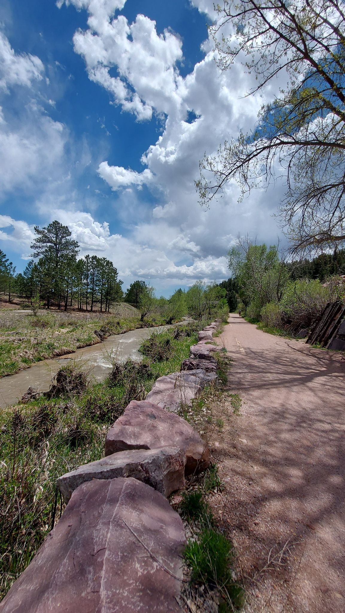 A dirt path alongside a rocky stream under a bright, cloudy sky. - New Santa Fe Regional Trail
