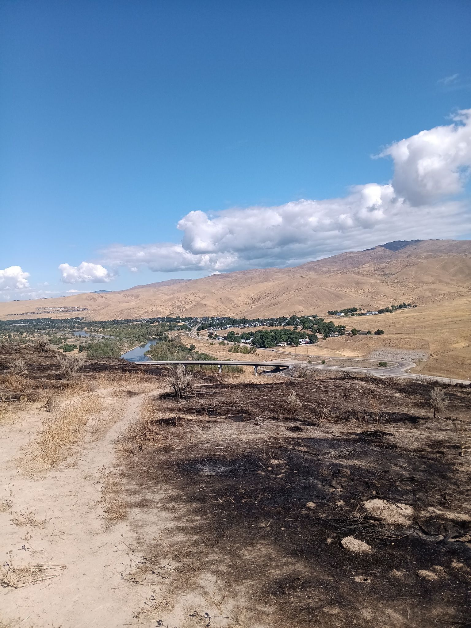 Burnt ground in foreground, distant town, river, and mountains under blue sky. - Ezra Meeker Loop