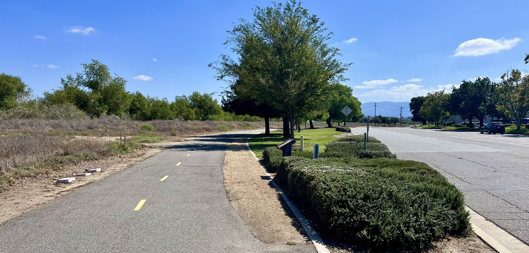 Paved path and road with green trees and bushes on a sunny day. - Temecula lookout and Murrieta Creek Bike Trail loop