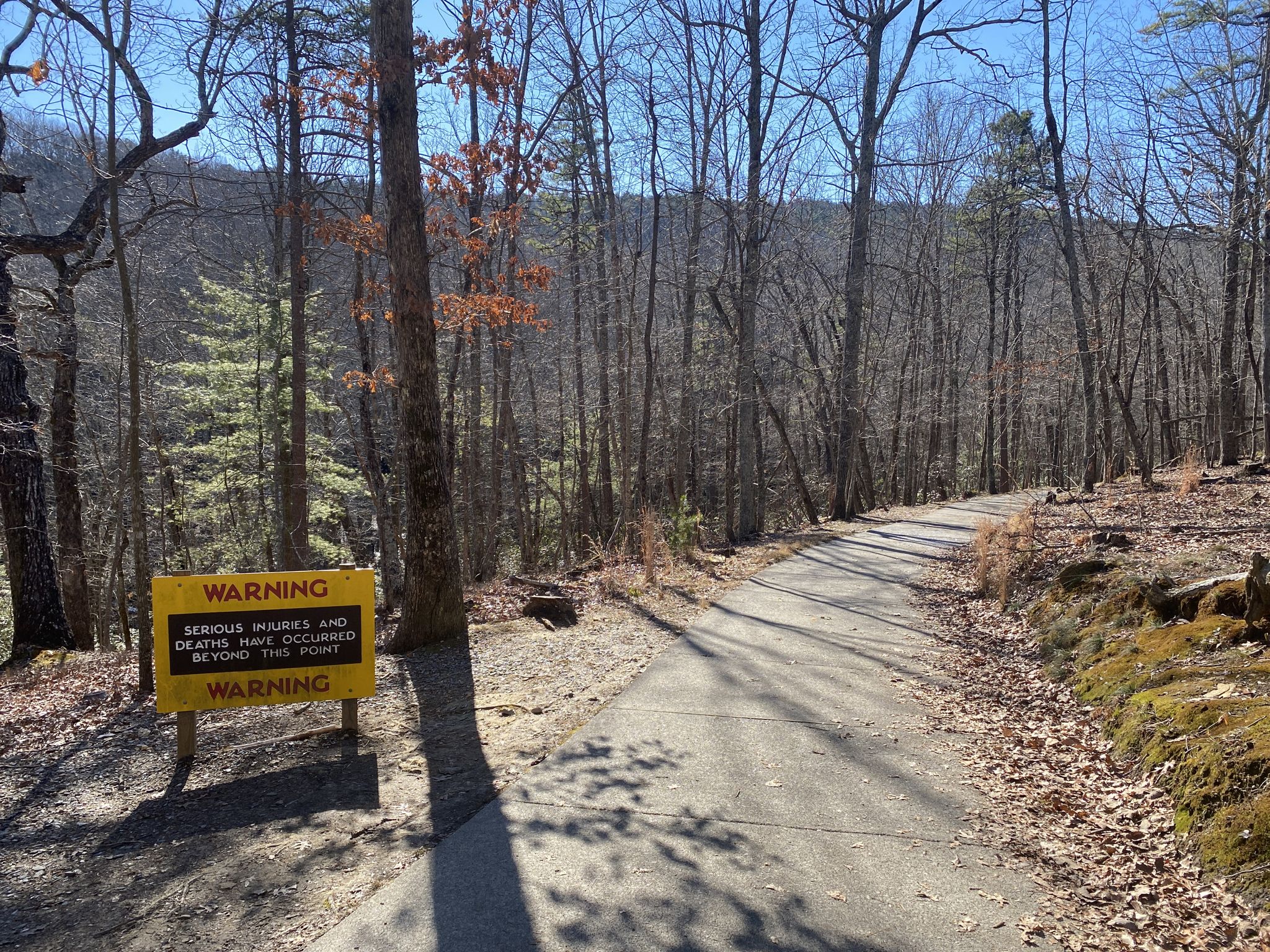 Paved path leading into a forest with a yellow warning sign. - Indian Creek Trail Loop
