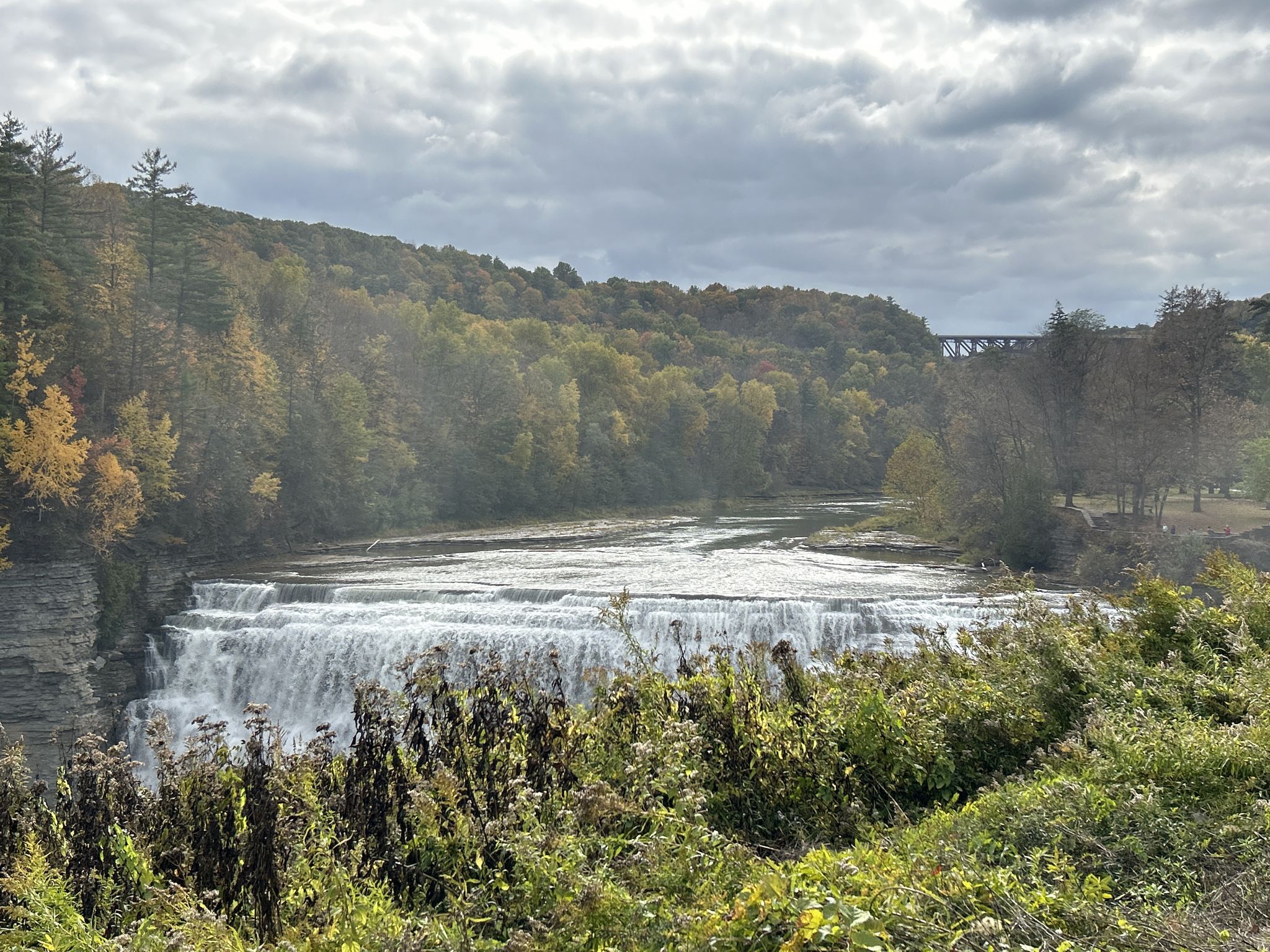 Wide waterfall cascading over rocks, surrounded by autumn foliage under cloudy sky. - Inspiration Point and Lower Falls via Gorge Trail