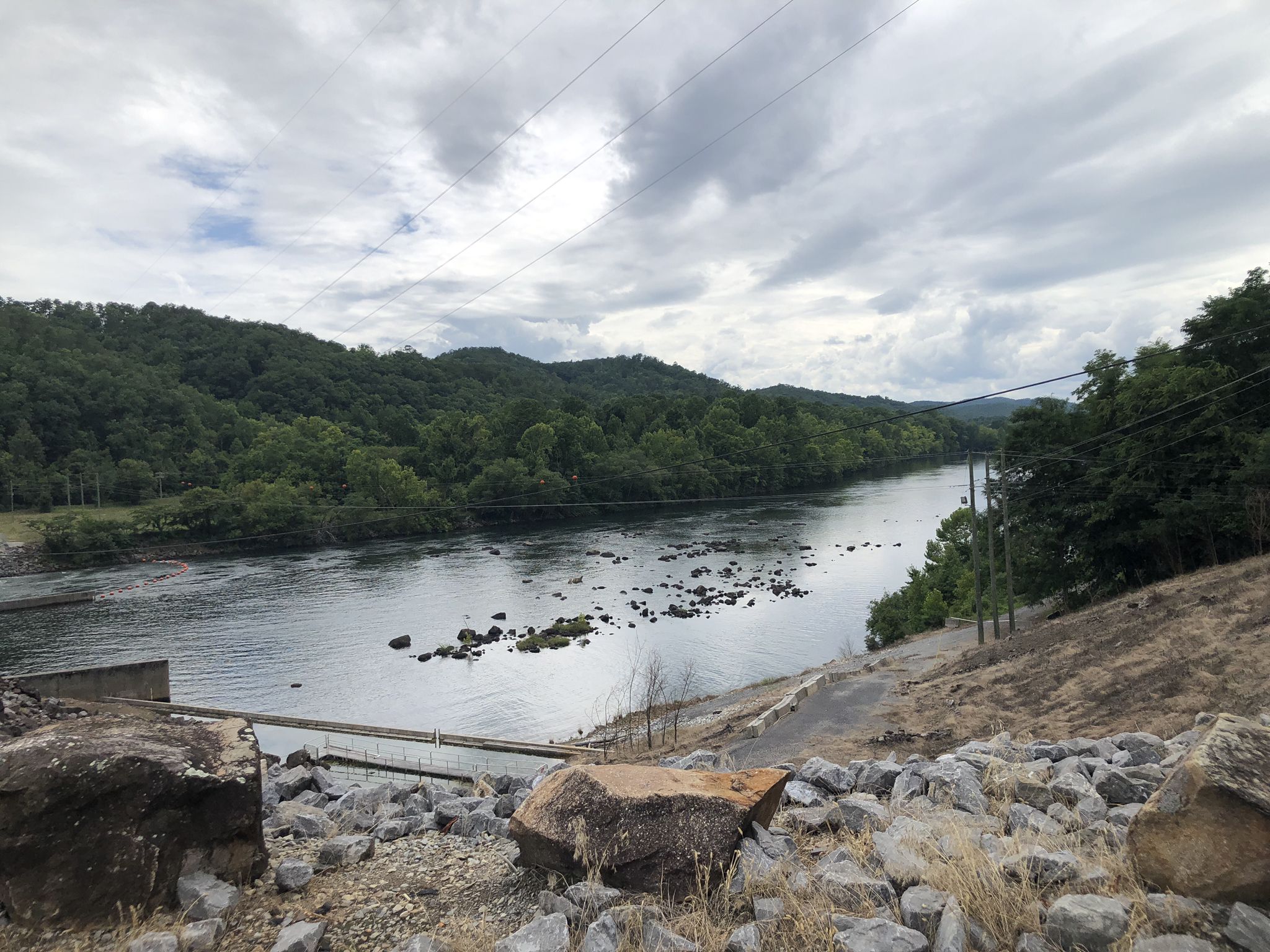 Wide river with rocky shallows, forested hills under an overcast sky. - Tail of the Dragon
