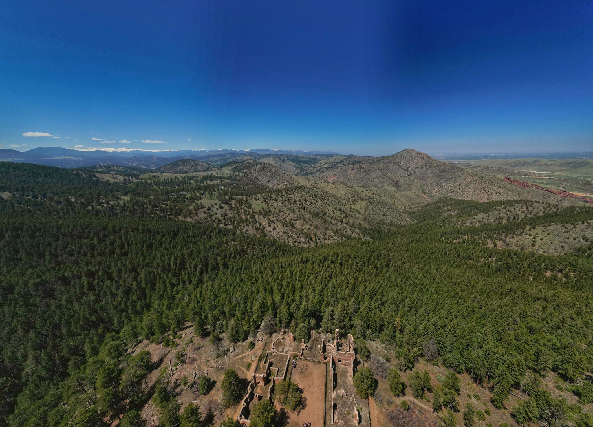 Aerial view of ancient ruins amidst vast green forests and distant mountains. - Bear Creek Trail