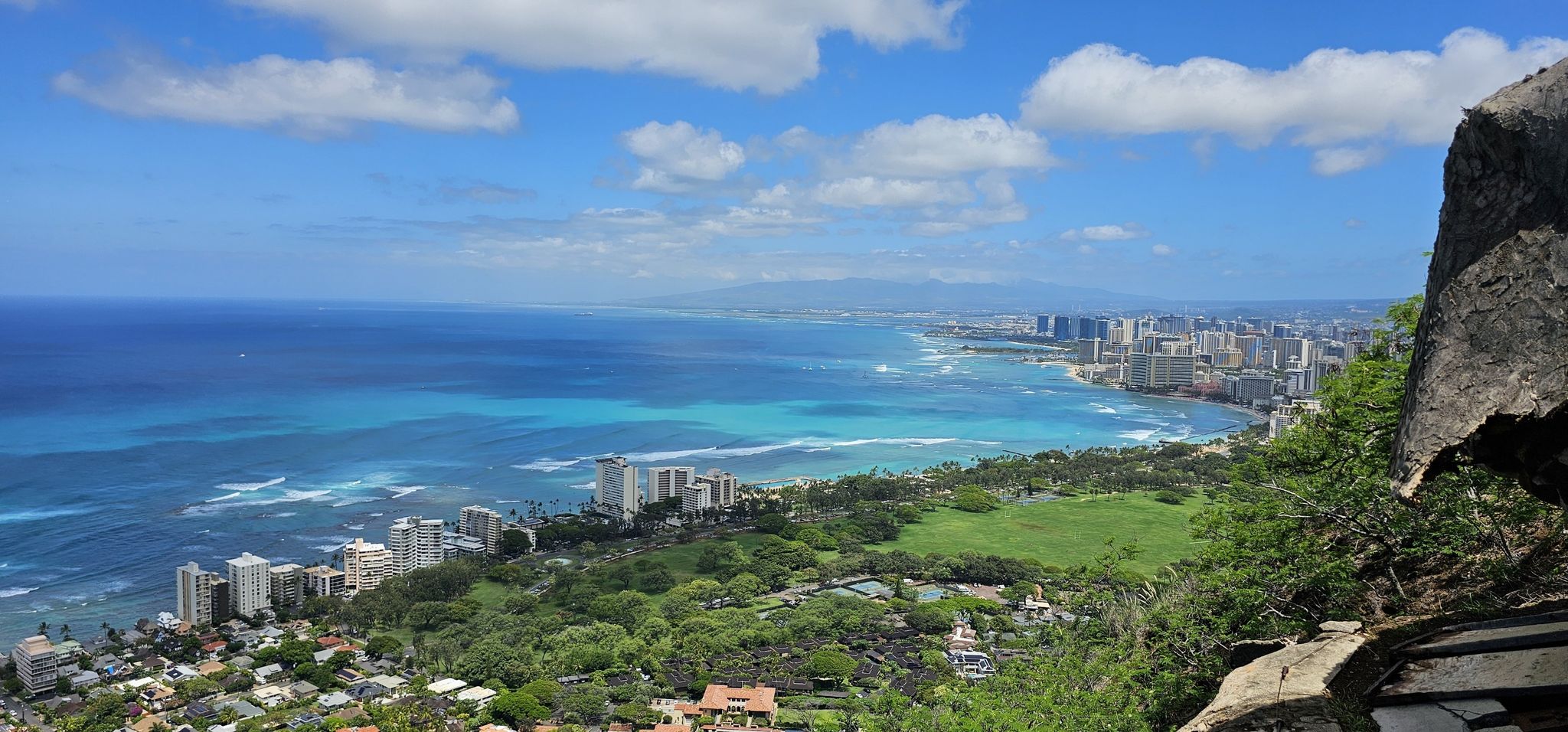 Coastal city view from a rocky outcrop, with blue ocean and white clouds. - Diamond Head loop from Waikiki