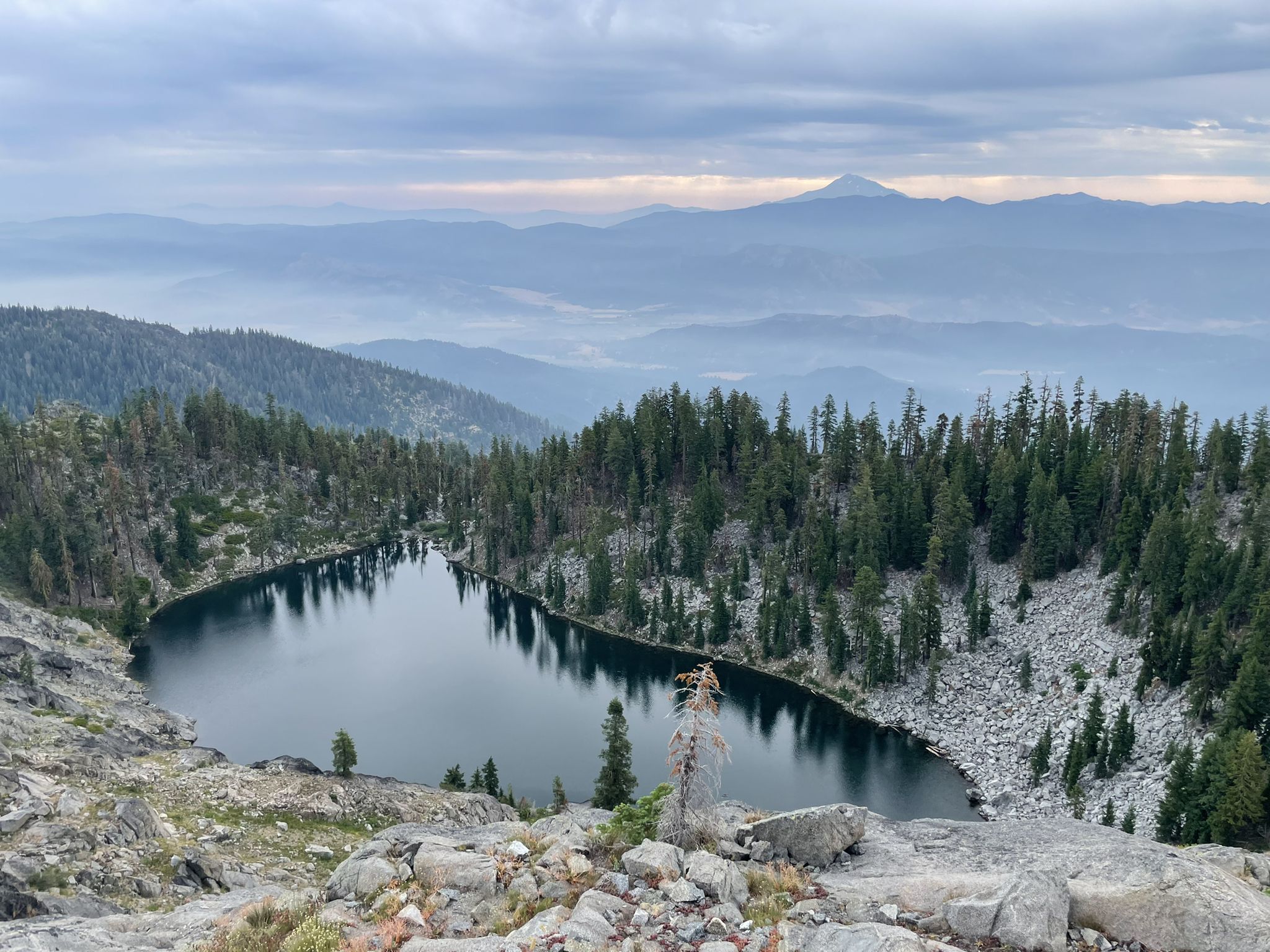 Dark lake surrounded by pine trees and rocky slopes under cloudy sky. - Paynes Lake via Pacific Crest Trail