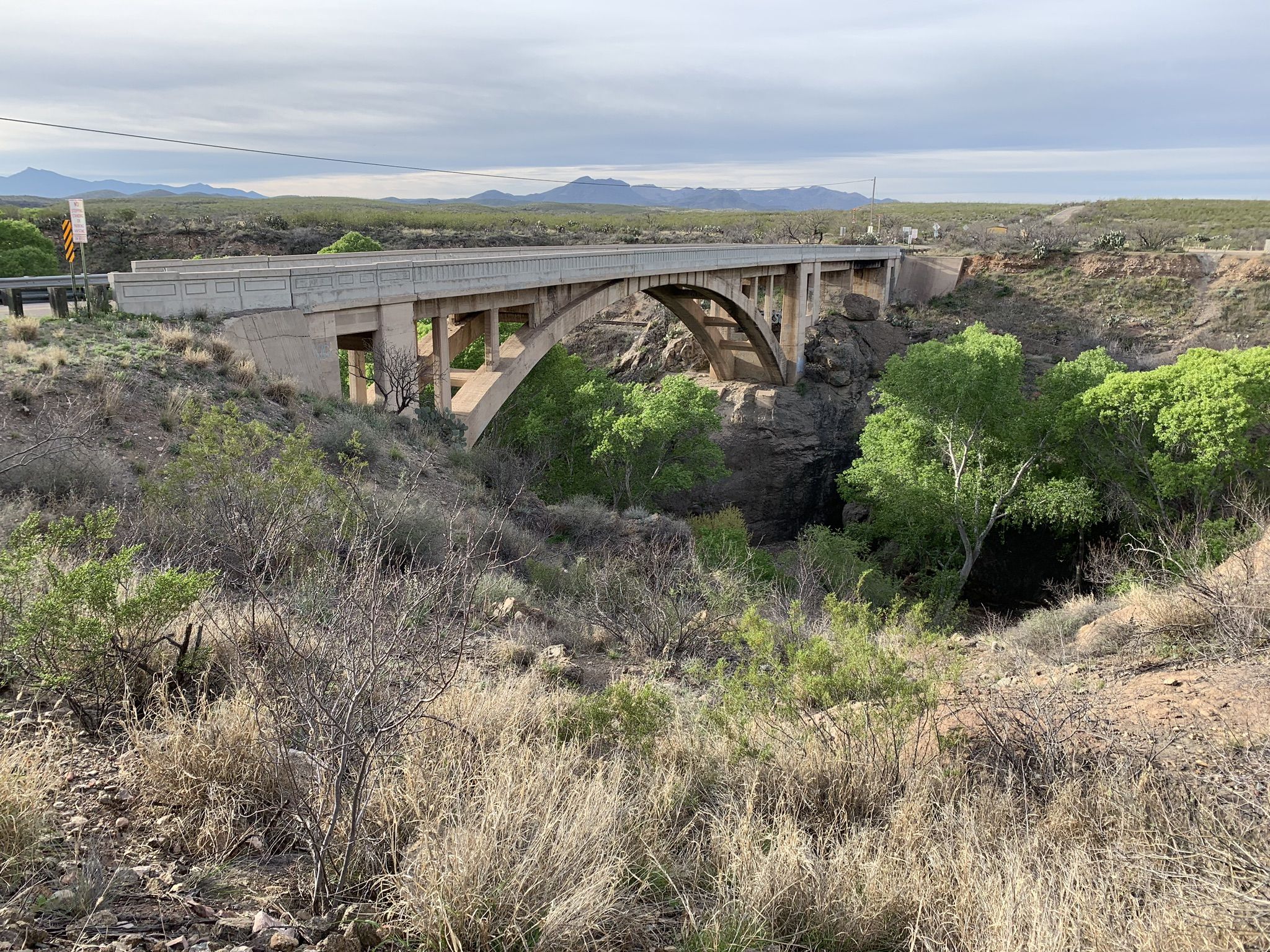 Concrete bridge spanning a dry riverbed with green trees below under overcast sky. - Las Cienegas – Cienega Creek Natural Preserve loop from Missile Tank