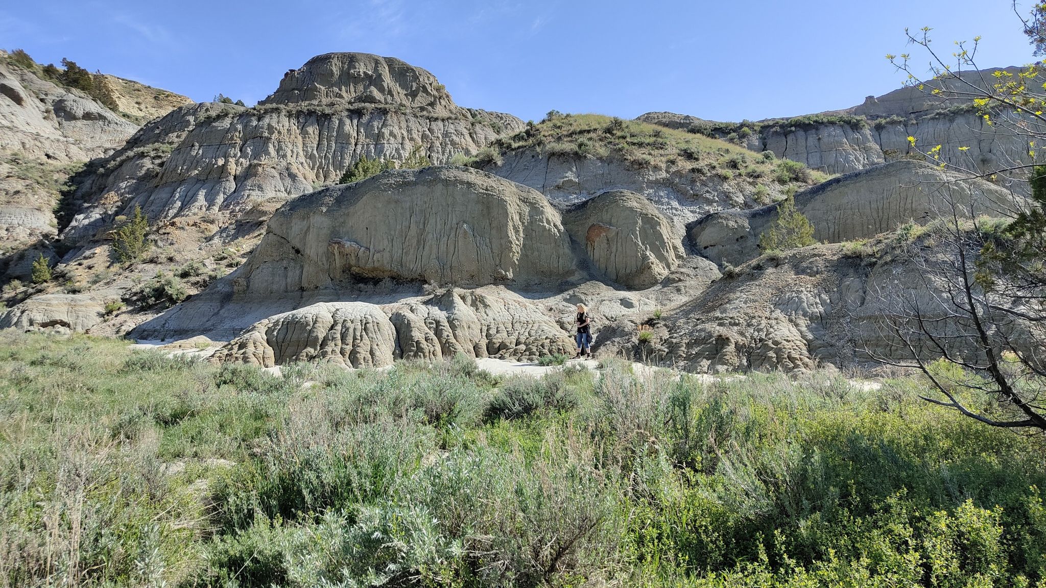 Person hiking on a sunny day amidst large, layered rock formations. - Caprock Coulee Trail