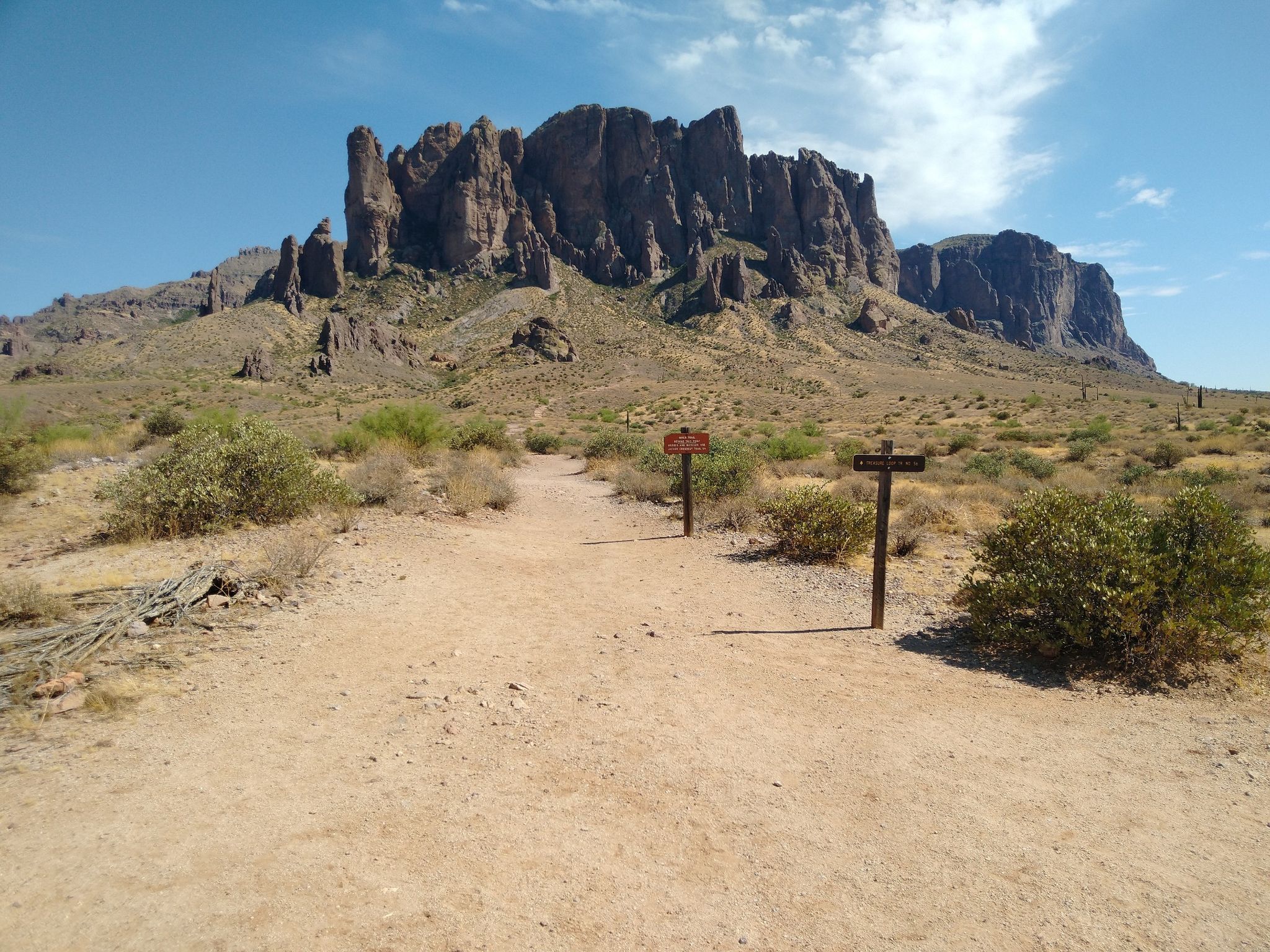 Desert trail forks with two signs, leading towards large rugged mountains. - Jacob's Crosscut, Prospector's View and Treasure Loop