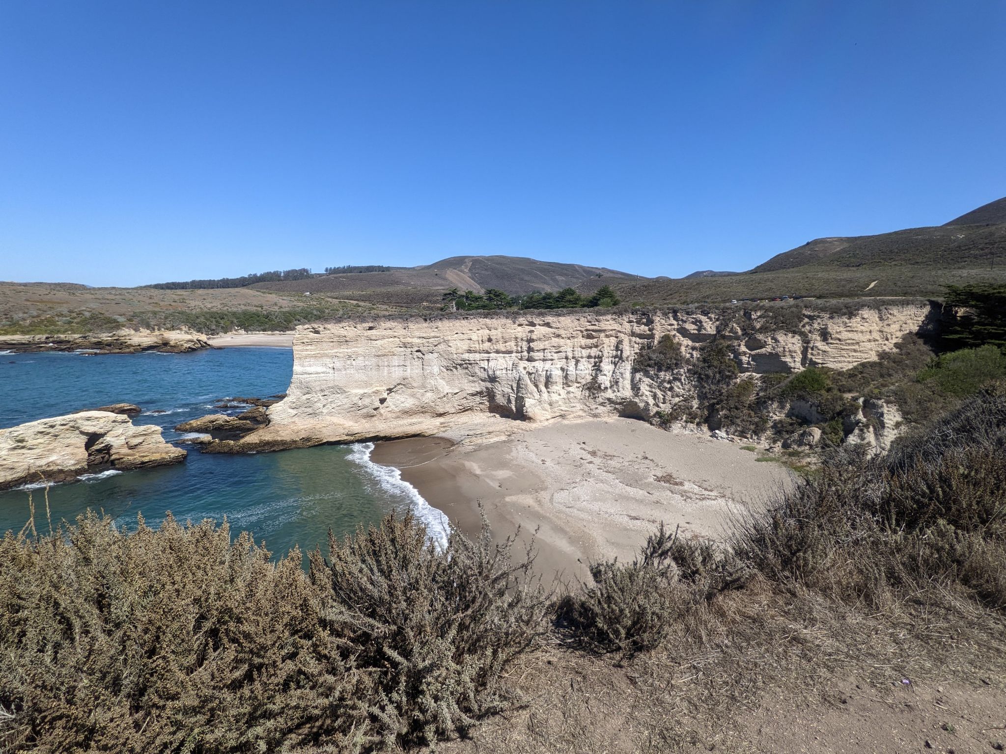 Sunny cove with a sandy beach, turquoise water, and tall cliffs. - Montaña de Oro Bluff Trail