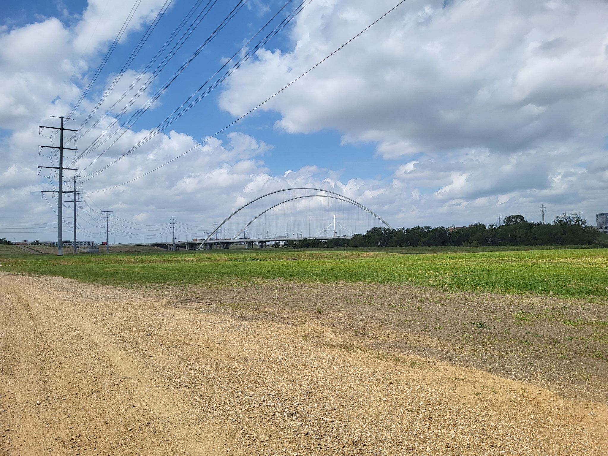 Dirt and grass field leading to a distant white arched bridge. - Katy Trail – Ridgewood Trail loop from Dallas Zoo