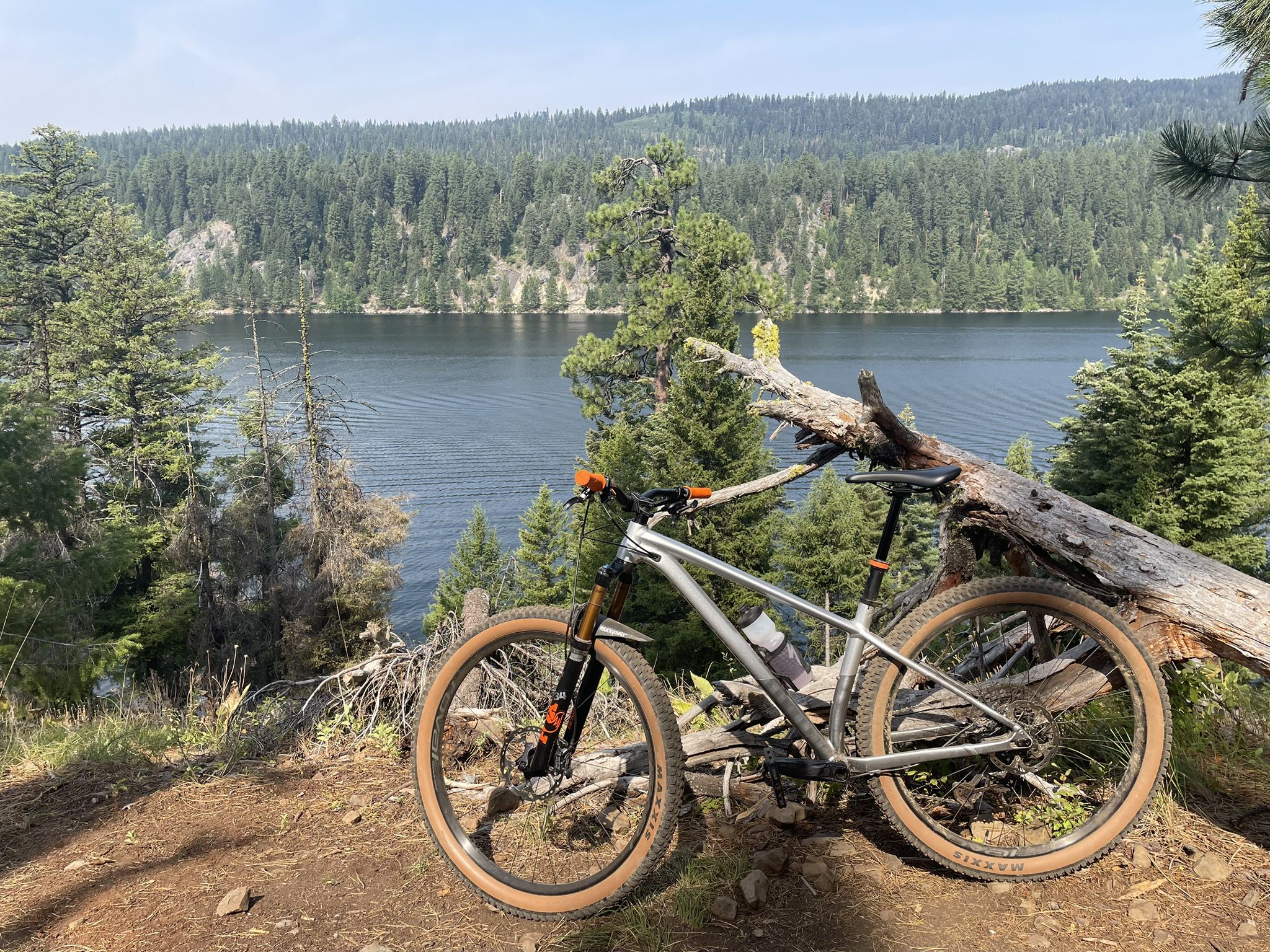 A mountain bike leans against a log, overlooking a lake and forested hills. - Huckleberry Trail – Payette Lake loop from RV Campground
