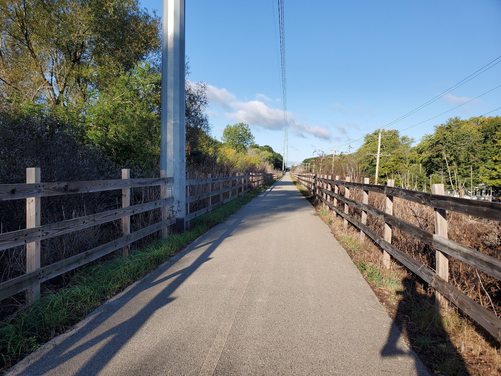 Paved path bordered by wooden fences under a sunny sky, person's shadow. - Running loop from Meadowbrook Park & Ride