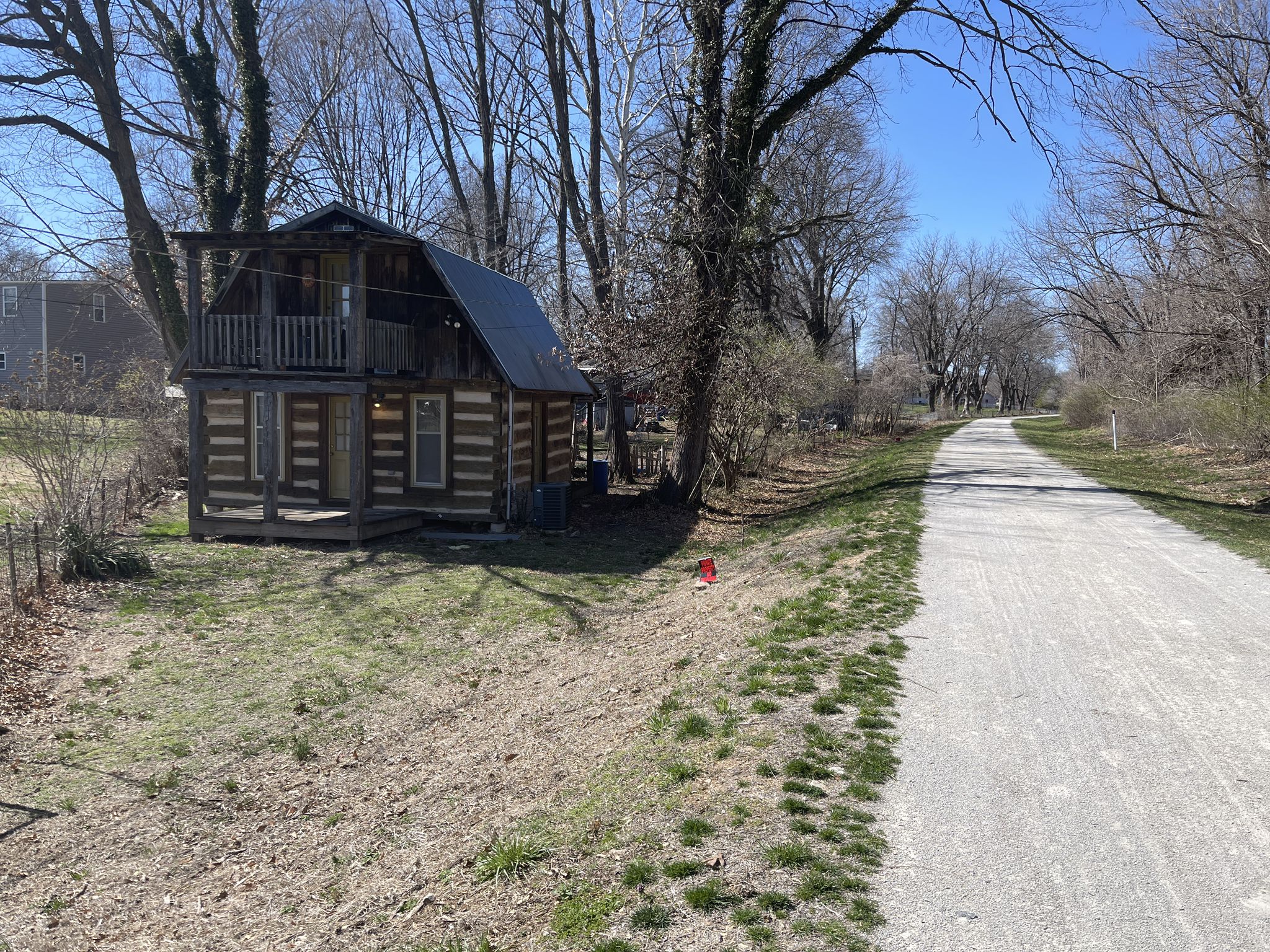 Small wooden cabin with a balcony next to a gravel path on a sunny day. - Rock Island Trail
