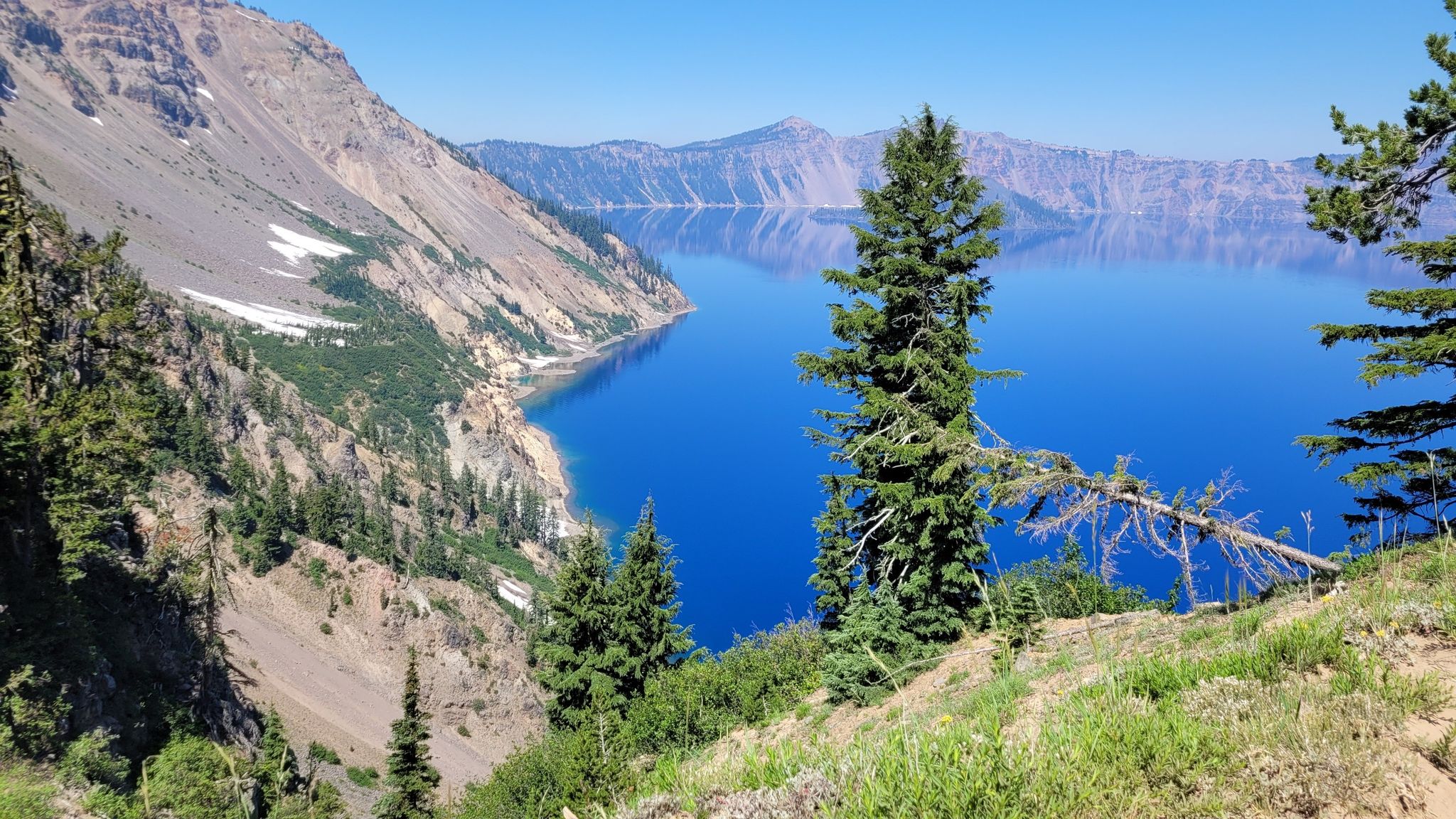 Bright blue lake surrounded by steep, rocky, forested slopes under clear sky. - Sun Notch Trail