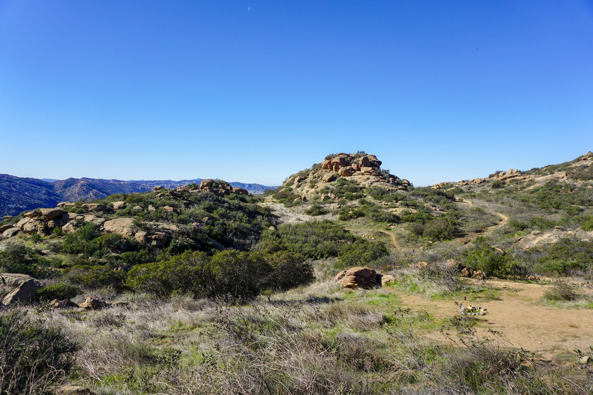 Sunny view of rocky, brush-covered hills with a clear blue sky and dirt path. - Hummingbird Trail Loop