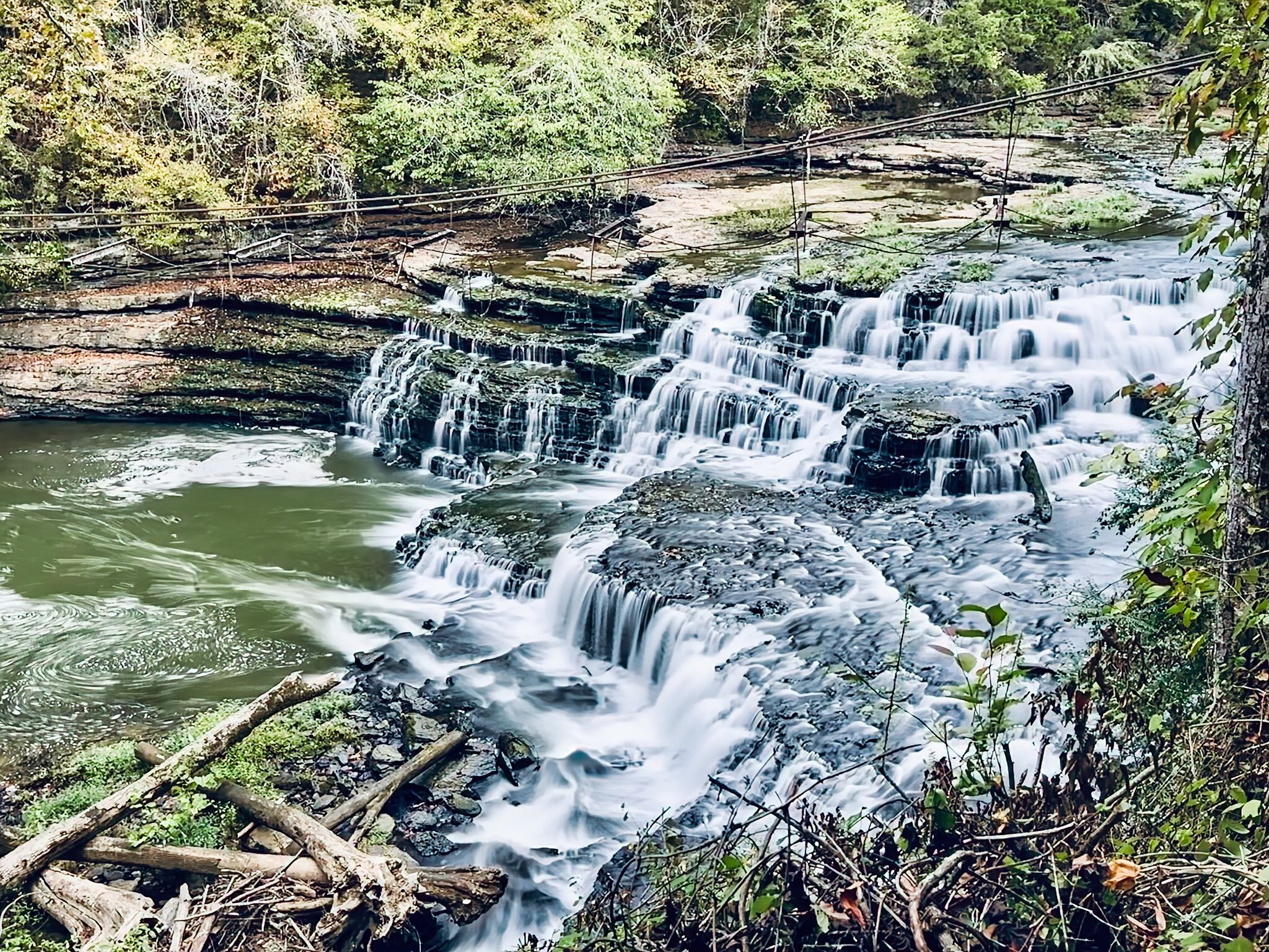 Wide, multi-tiered waterfall flowing into a green river, surrounded by trees. - River and Ridgetop Trail Loop