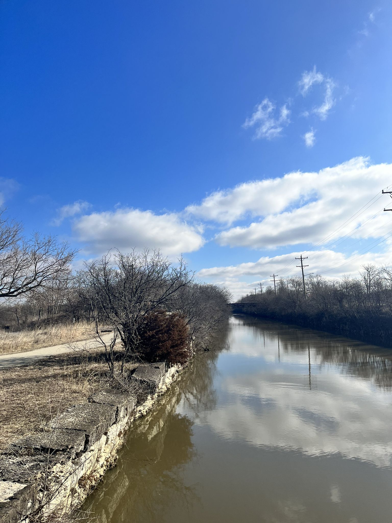 A canal with reflections under a bright blue sky with white clouds. - Heritage Quarries Recreation Area loop