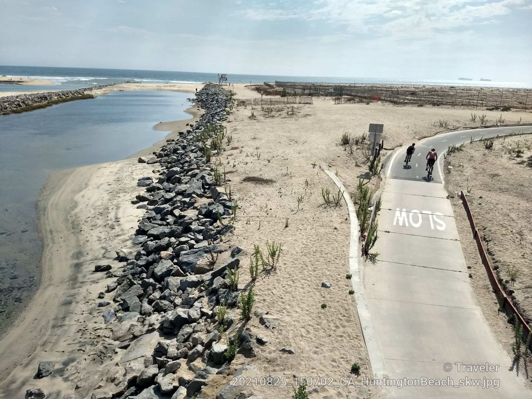 Two cyclists on a paved path next to a sandy beach and water channel. - Santa Ana River Trail