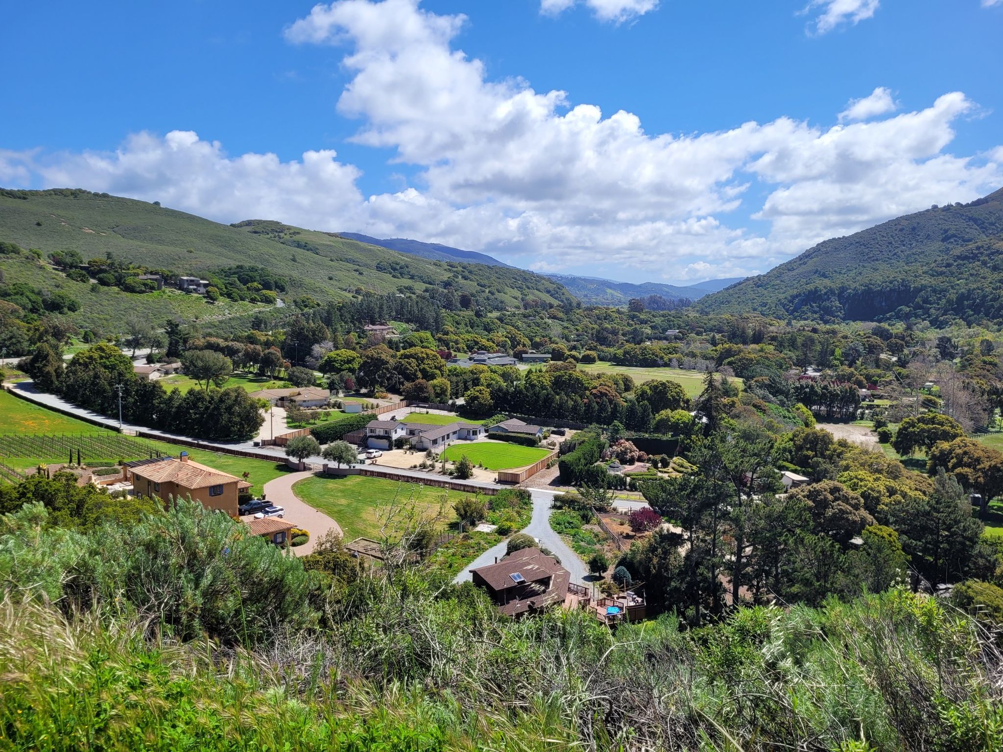 A sunny valley with green hills, scattered houses, and a blue sky. - West Carmel River Valley Road – Top of the Cachagua Road Climb loop from Garland Ranch Regional Park
