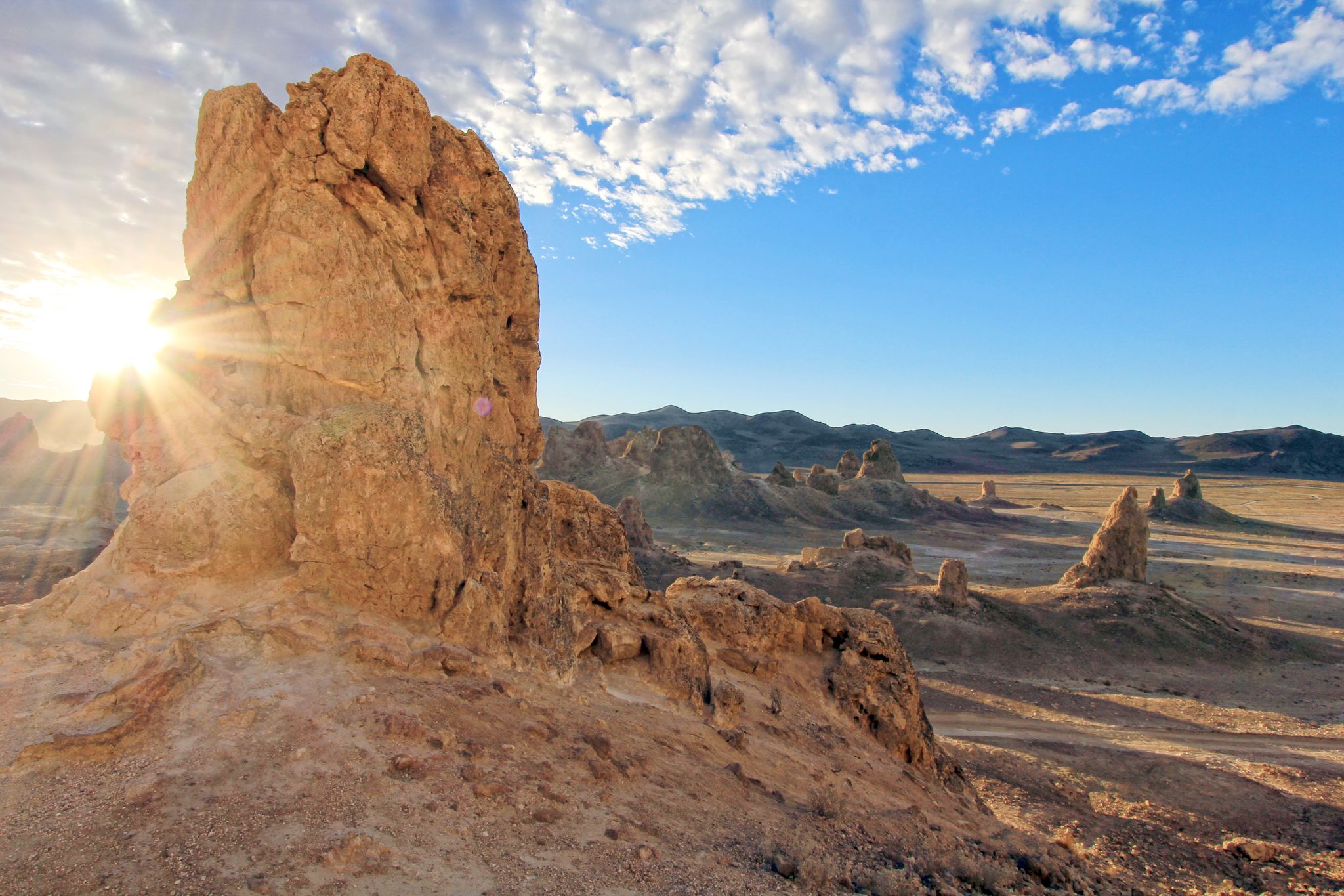 Sunburst behind a large rock formation in a desert with distant mountains. - Trona Pinnacles loop from Trona Pinnacles