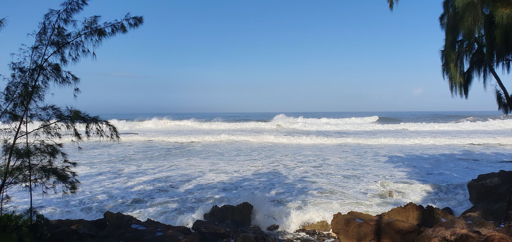 Powerful ocean waves crash onto a rocky shore under a clear blue sky. - Kulalua – Shark's Cove loop from Waimea Bay