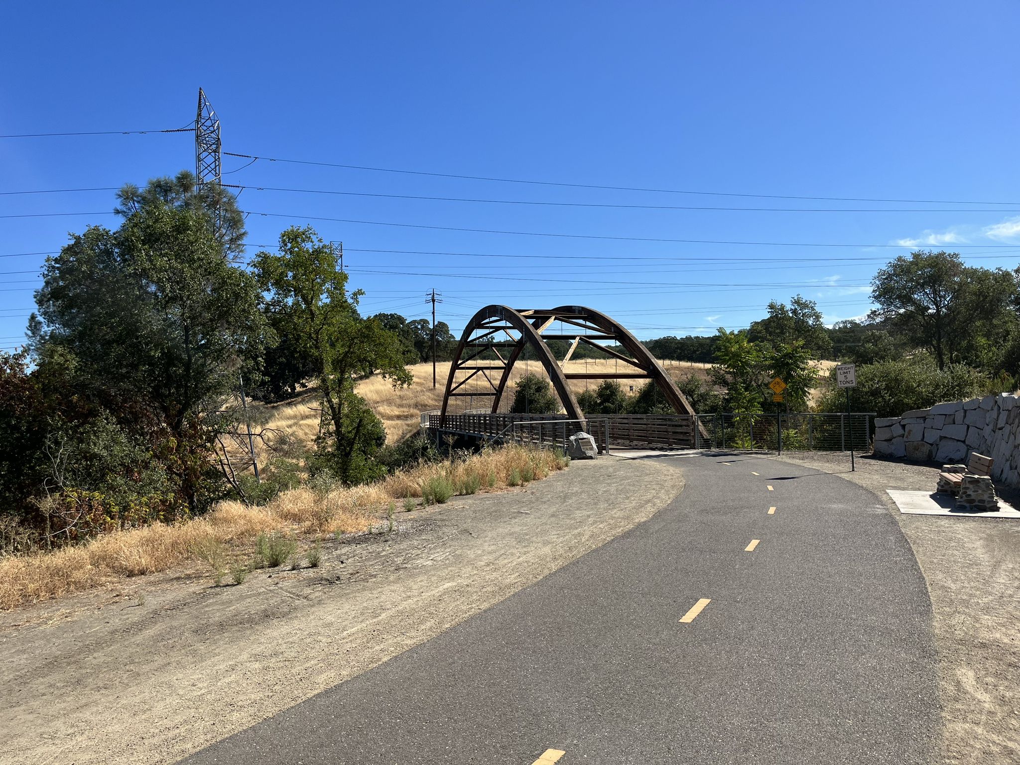 Paved path leading to a modern arch bridge over a dry landscape under blue sky. - Johnny Cash and Oak Parkway Trails