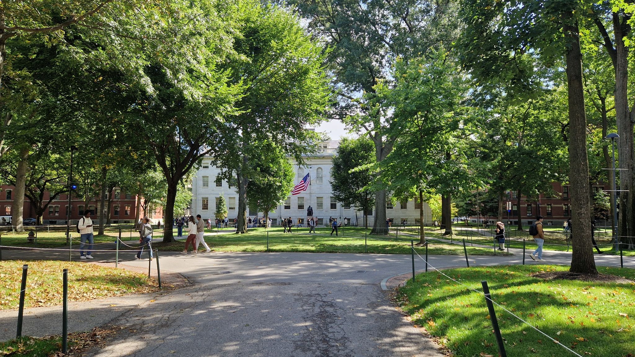 Sunny day with a white building, green trees, and people walking outdoors. - Harvard Yard Tour