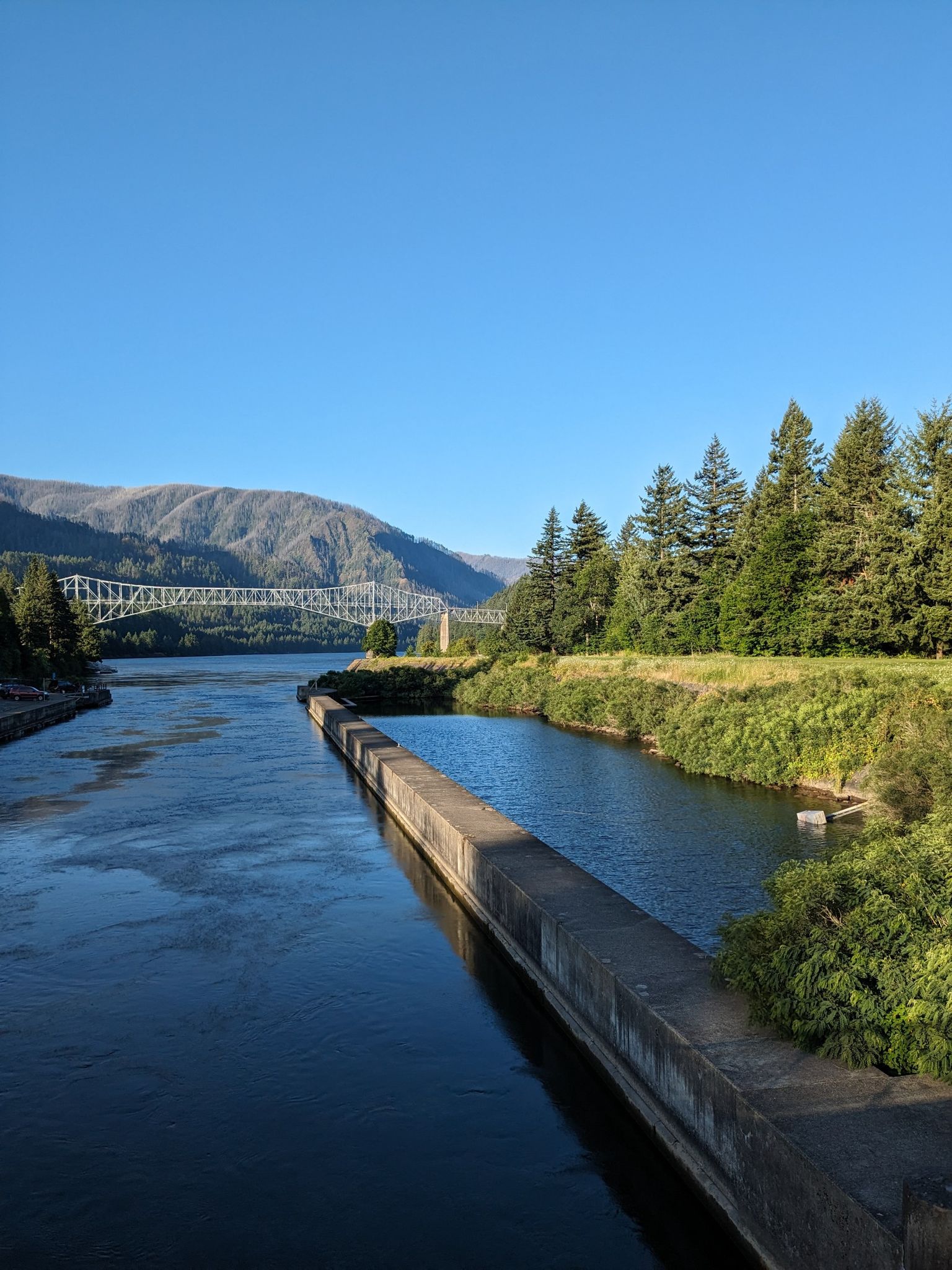 Wide river, concrete barrier, distant bridge, mountains under clear blue sky. - Historic Columbia River Highway State Trail