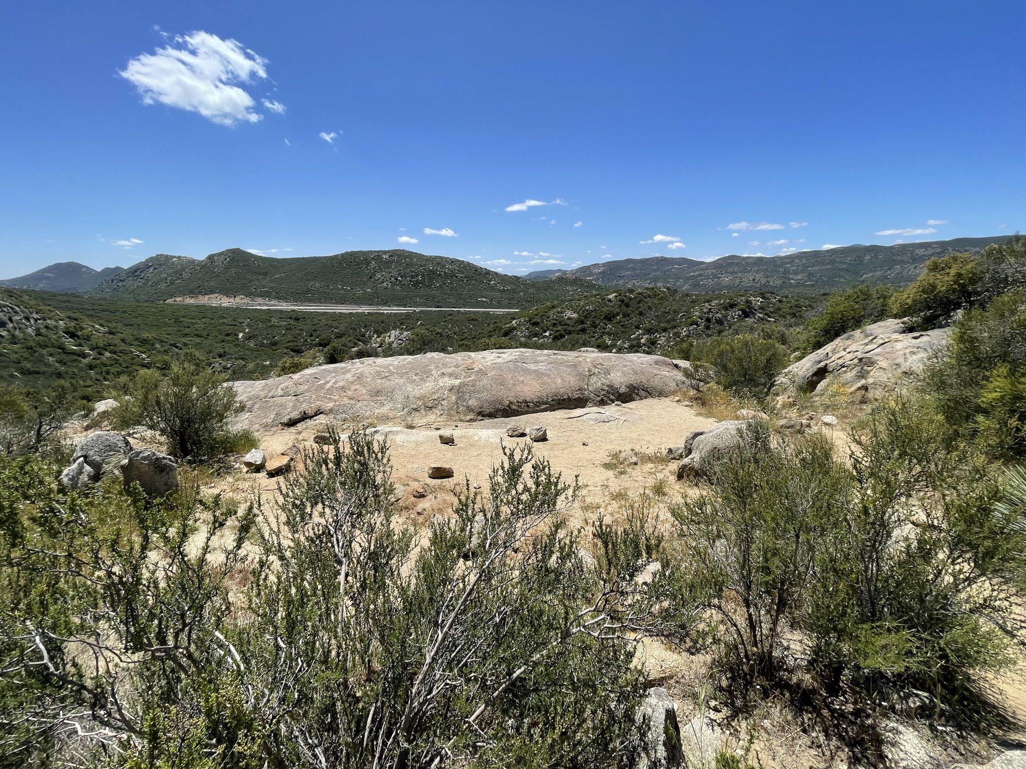 Sunny landscape with large rock formations, green brush, and distant mountains. - Kitchen Creek Falls Trail
