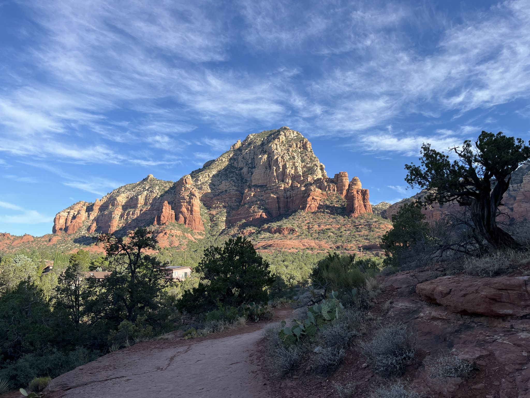 A dirt path leads to a large, rugged red rock mountain under a blue sky. - Thunder Mountain – MTB Trails in Sedona