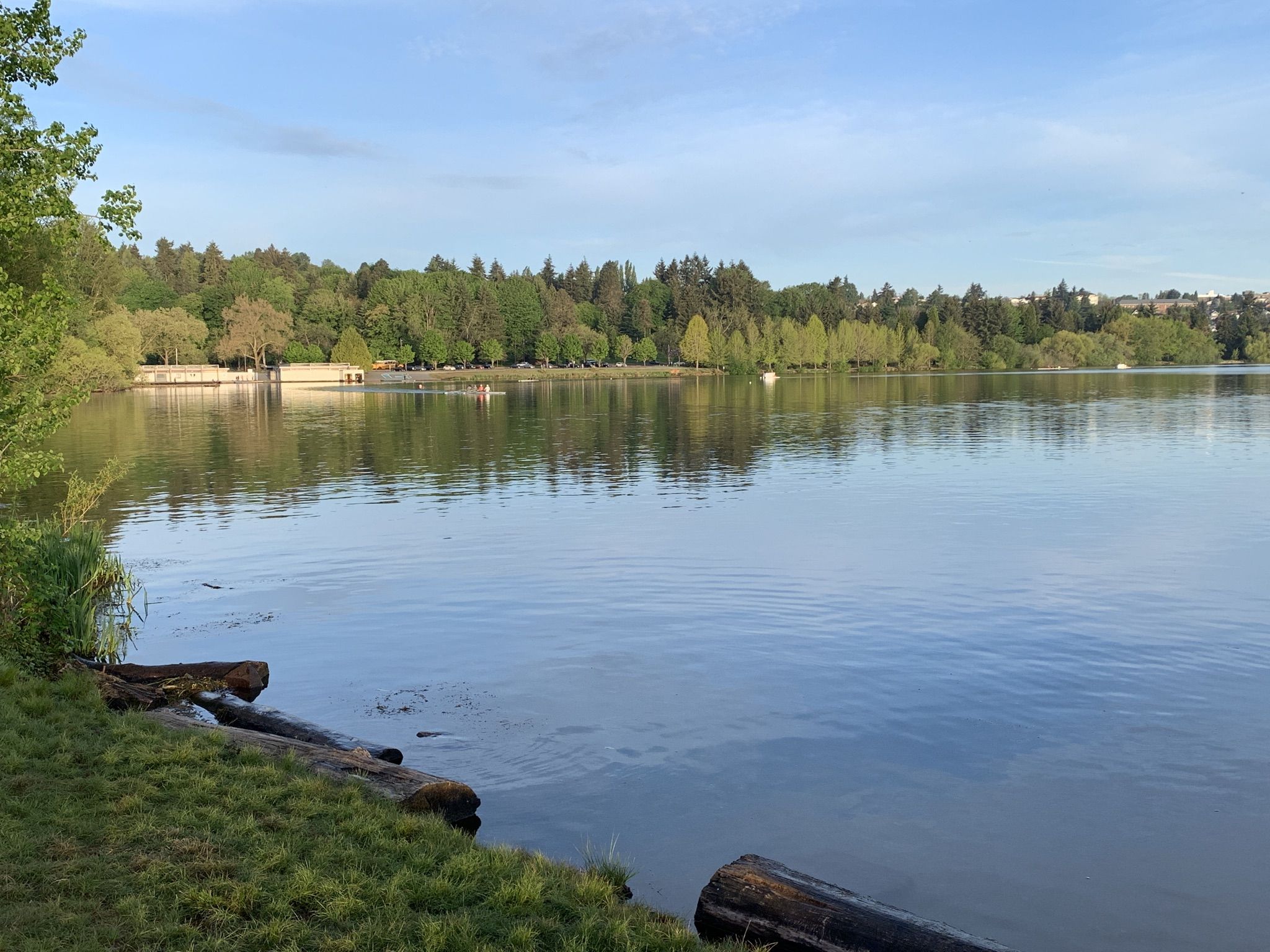 Calm lake reflecting distant trees and a few people on the far shore. - Green Lake Outer Loop