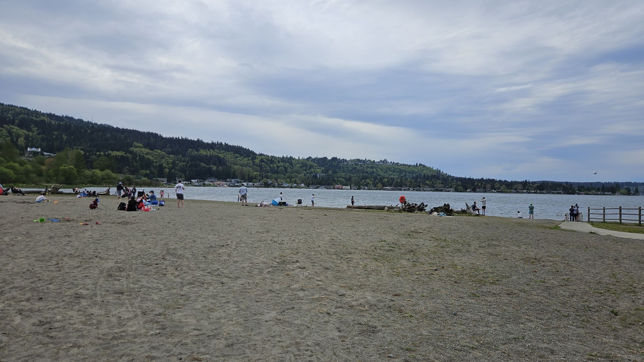 People enjoy a wide sandy beach with calm water under an overcast sky. - Tibbetts Creek Trail
