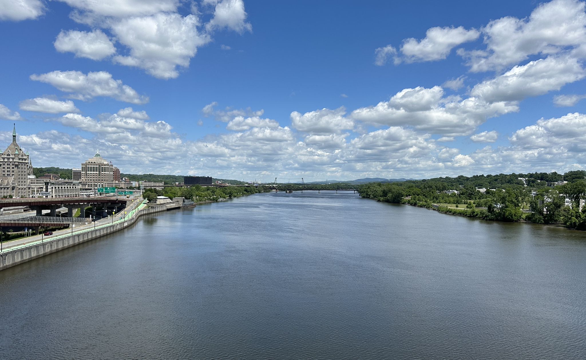 A wide river flows past a city and green hills under a cloudy sky. - Albany to Mount Greylock loop via Albany-Hudson Electric Trail