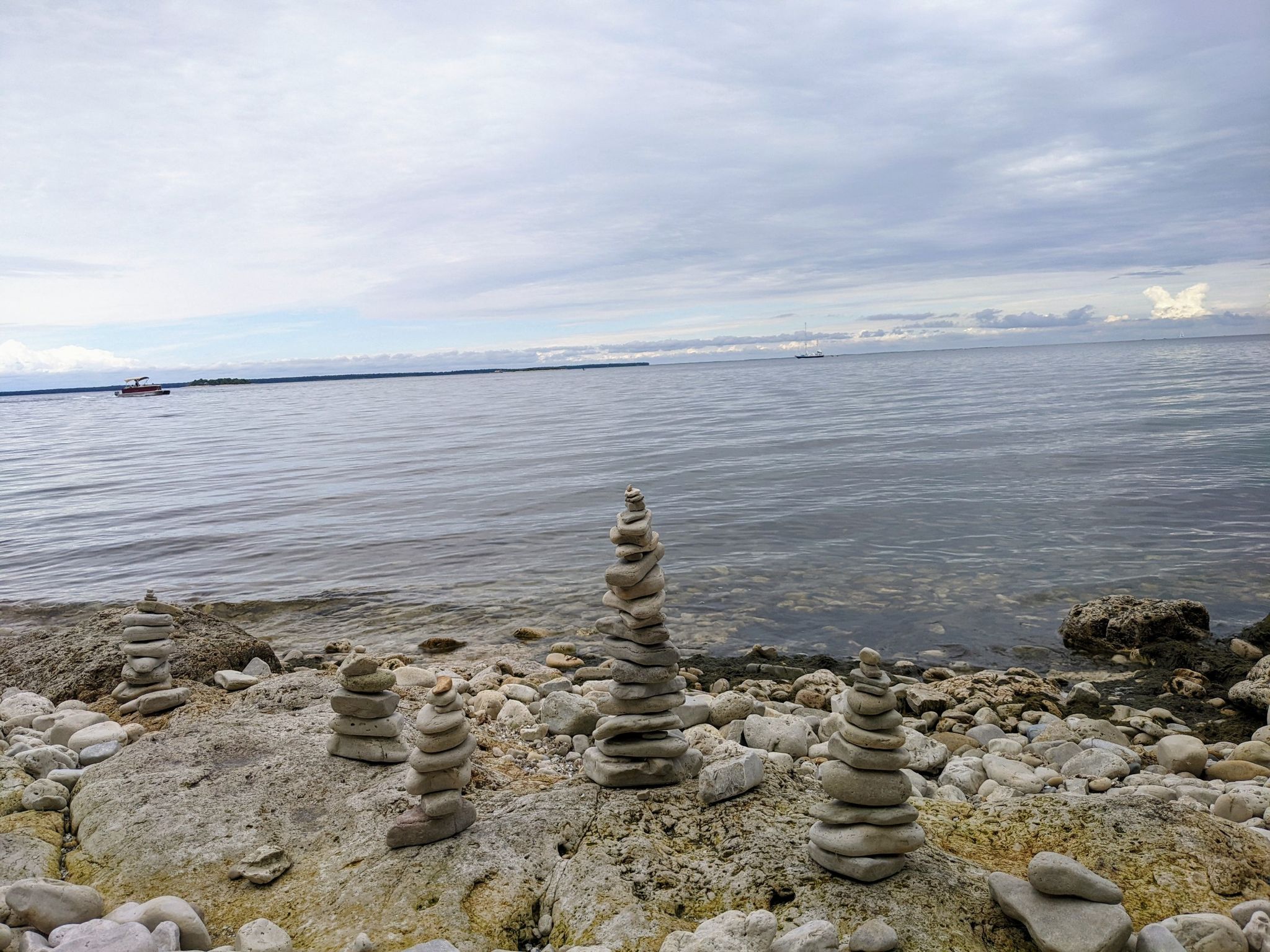 Stone cairns on a rocky beach with calm water under a cloudy sky. - Fish Creek Running Trail – Eagle Bluff Lighthouse loop from Fish Creek