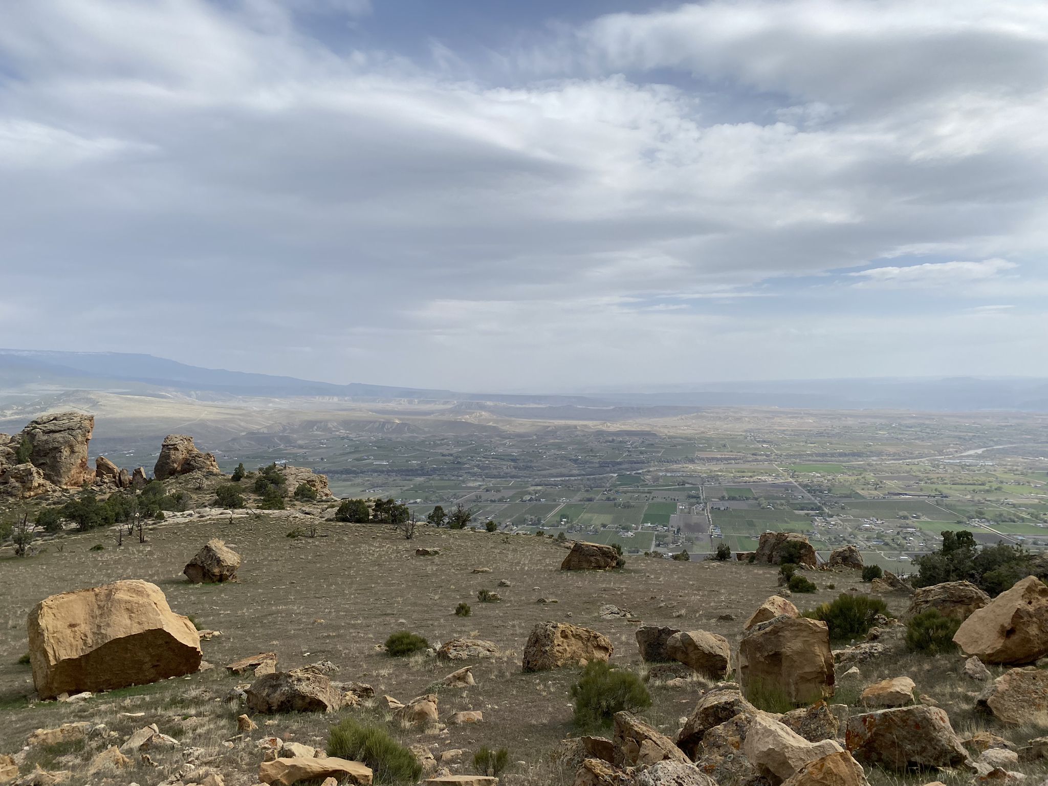 Rocky foreground overlooks a vast green valley under an overcast sky. - Mount Garfield Trail