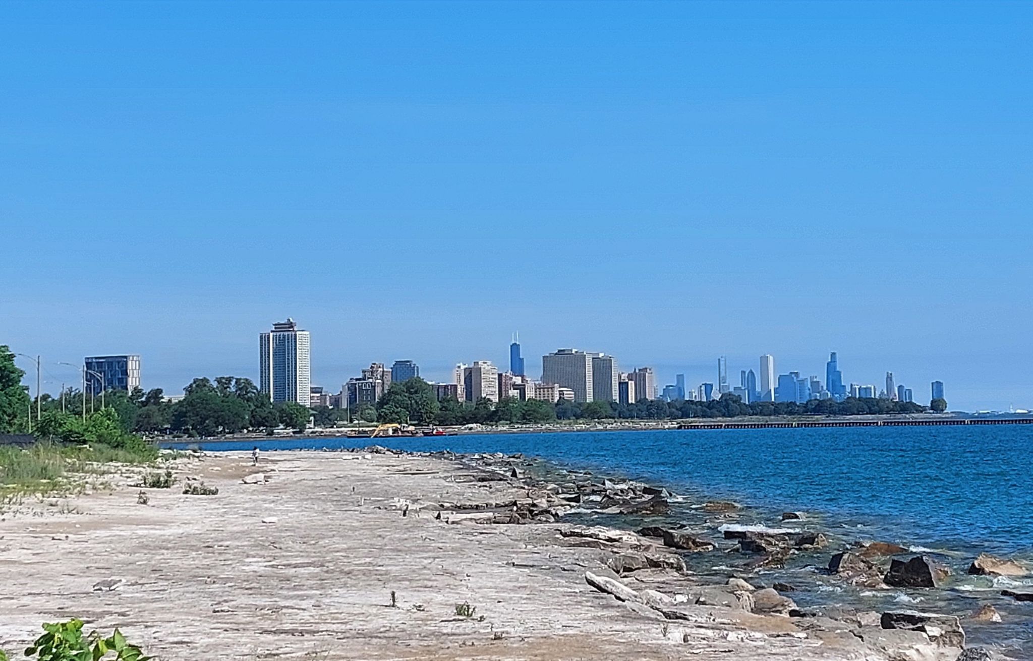Rocky shoreline and blue water, with a distant city skyline under clear sky. - 63rd St. Beach Dunes – Hyde Park loop from 91st Street (Chesterfield)