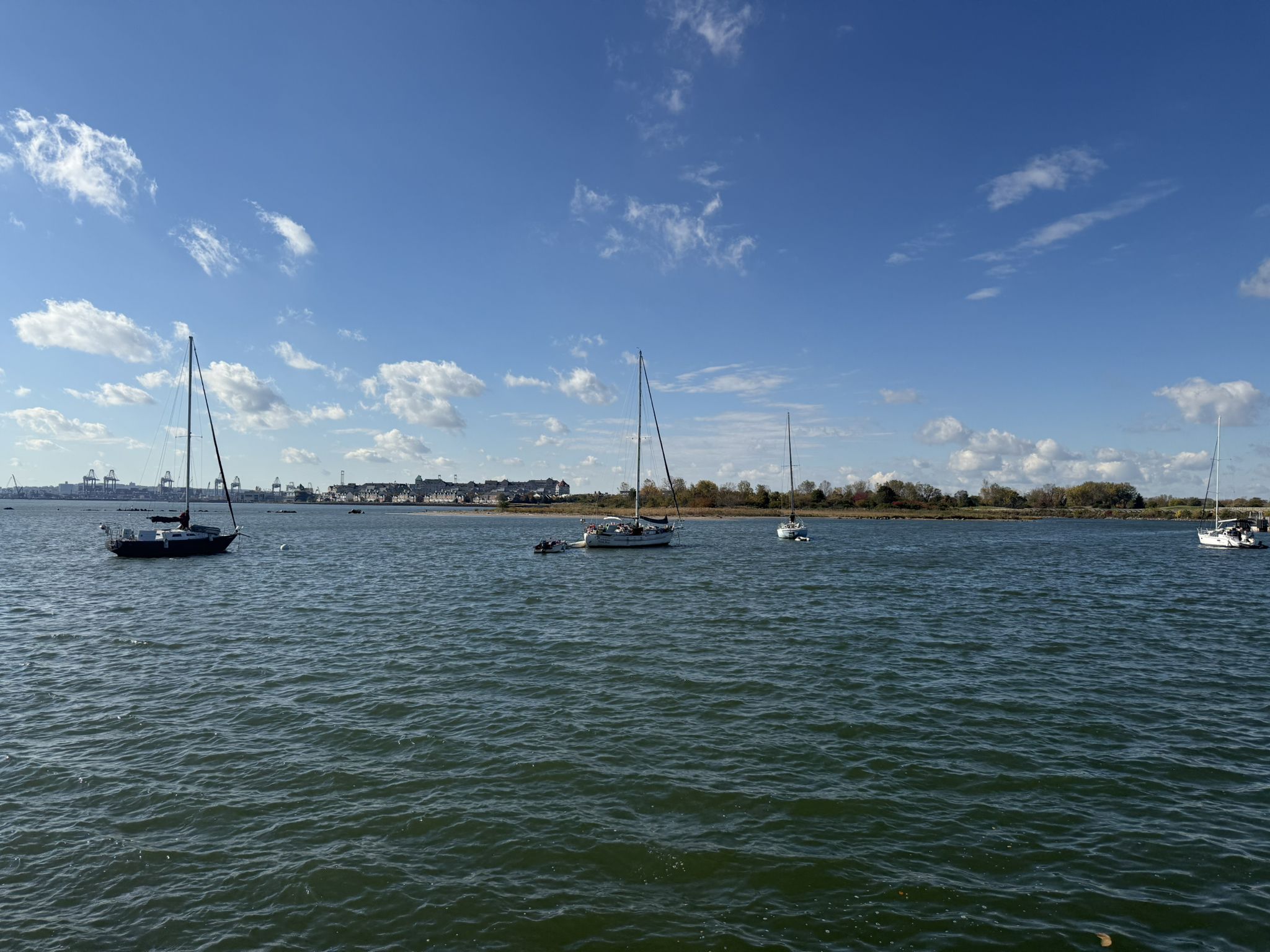 Several sailboats anchored on blue water under a bright, partly cloudy sky. - Caven Point Trail