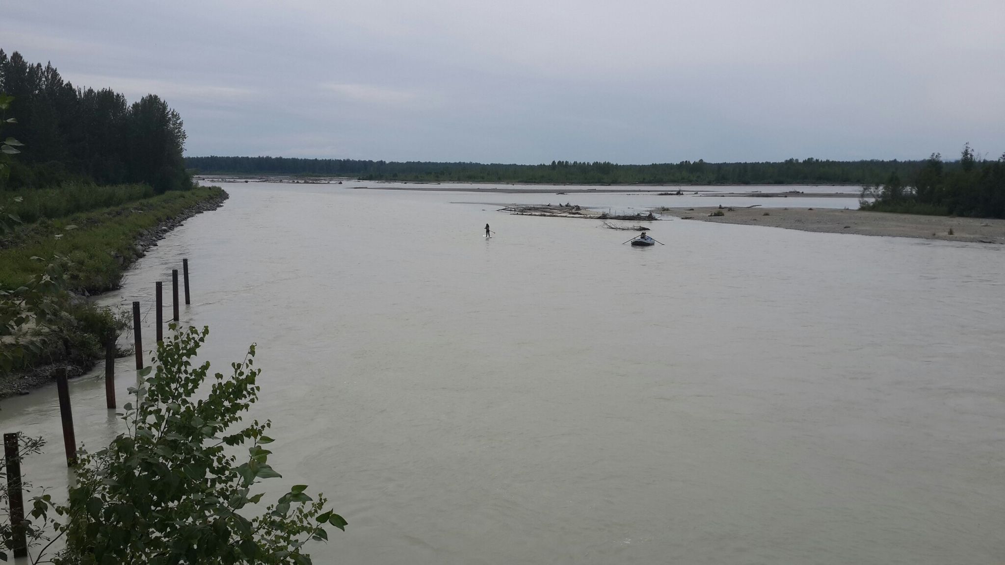 Wide, murky river with a person wading and a small boat under overcast sky. - Chase Trail