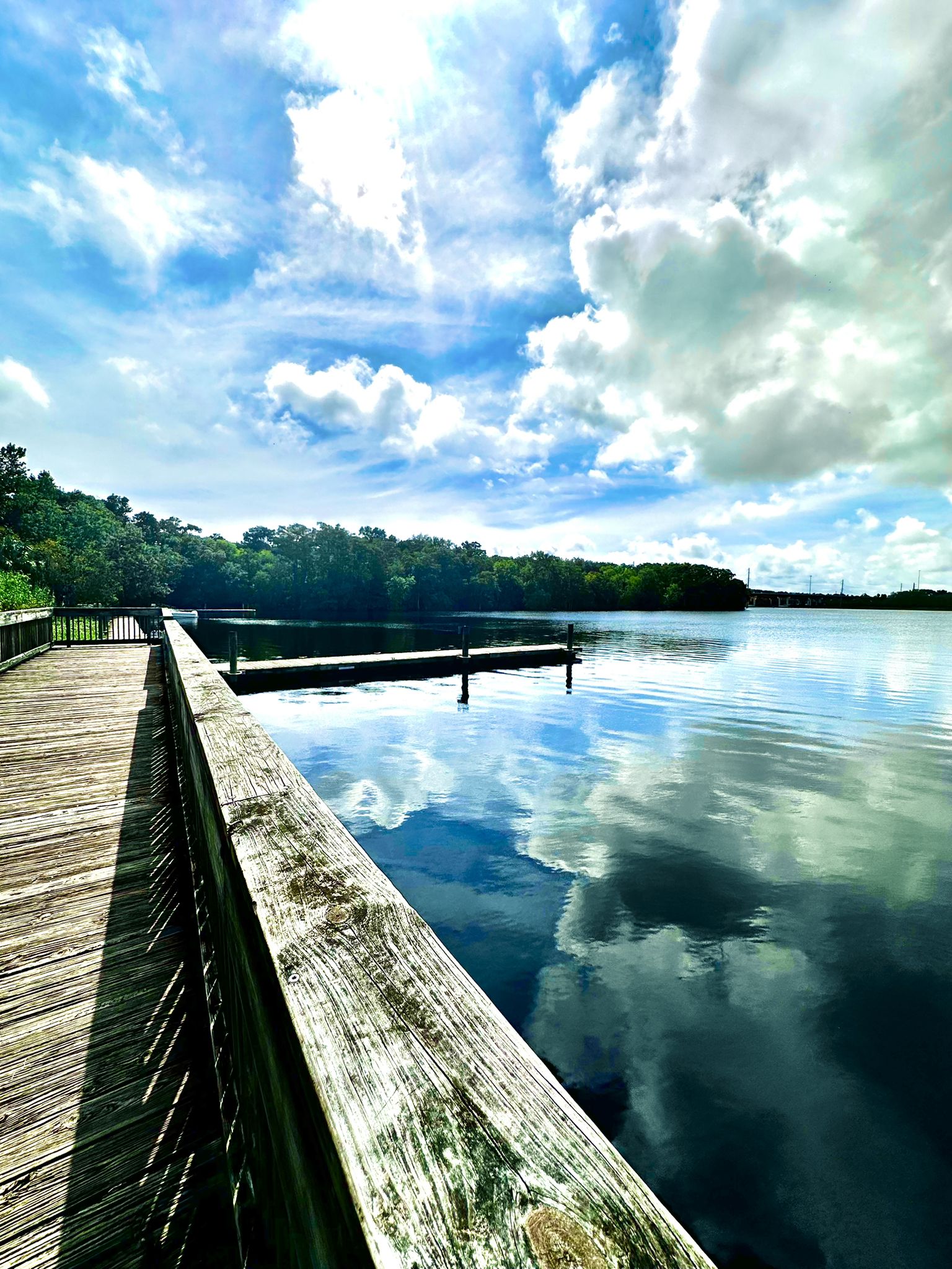 Wooden boardwalk next to a calm lake reflecting a bright, cloudy sky. - Spring-to-Spring Trail