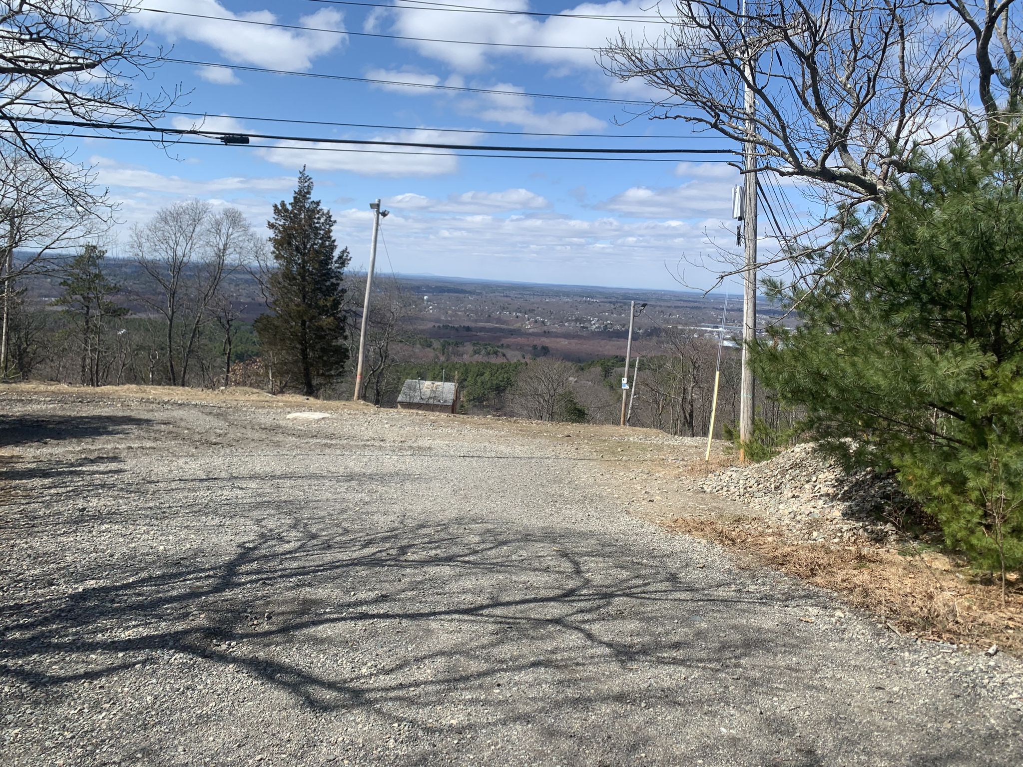 A gravel clearing overlooks a distant valley and town under a blue sky. - Summit Road – Summit Road loop from Eustis Estate Museum and Study Center